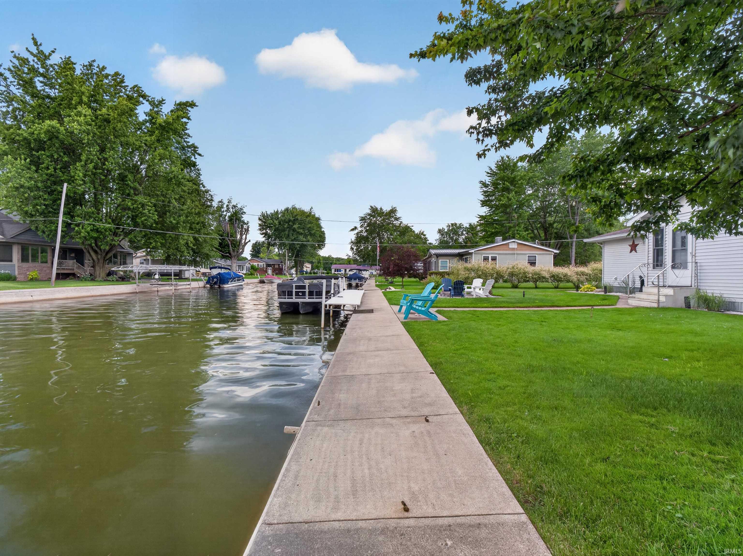 Waterfront property featuring a concrete dock, manicured lawn, and mature trees