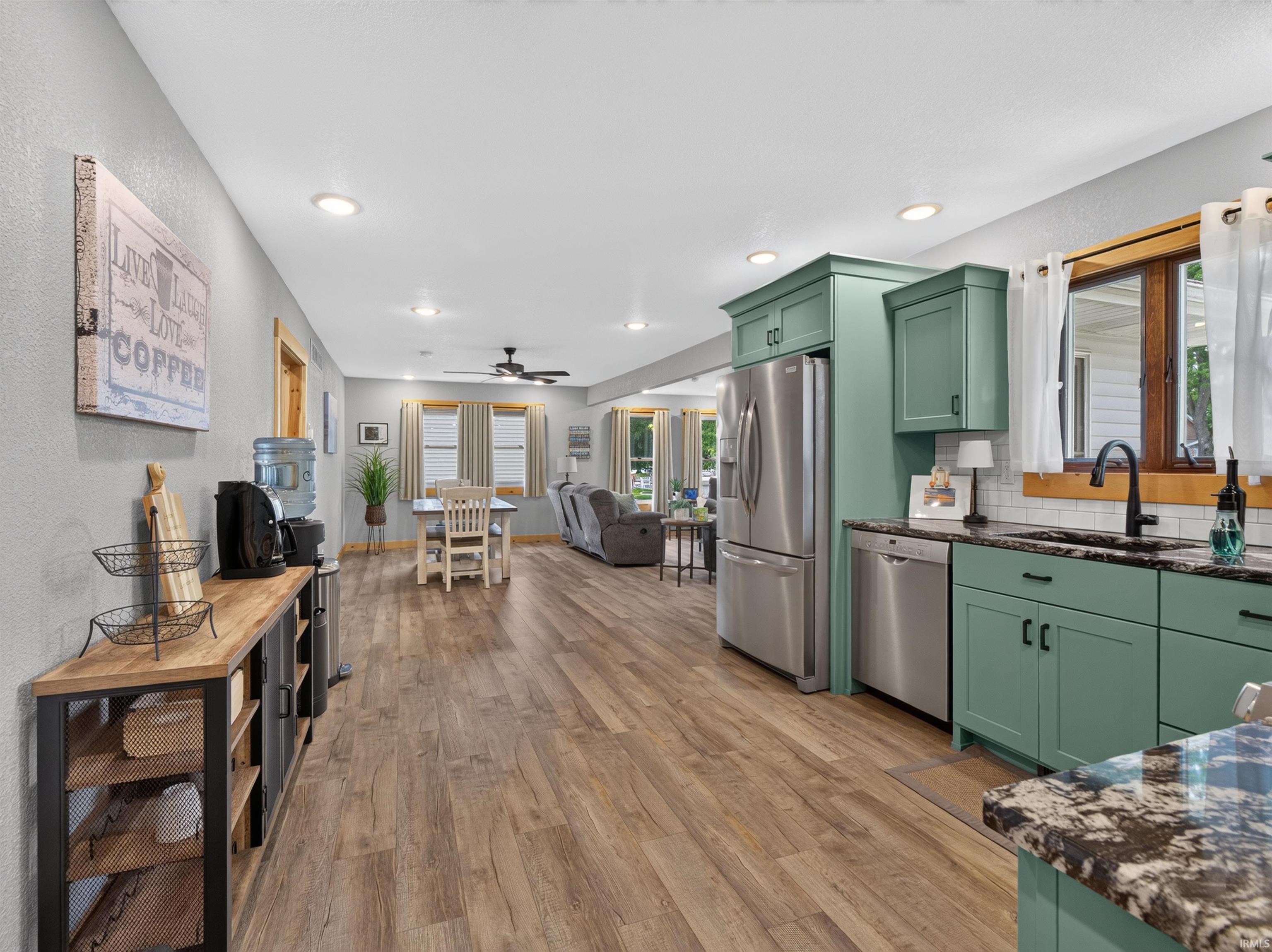 Kitchen area featuring green cabinetry, stainless steel appliances, dark stone countertops, a subway tile backsplash, and wood-finish flooring