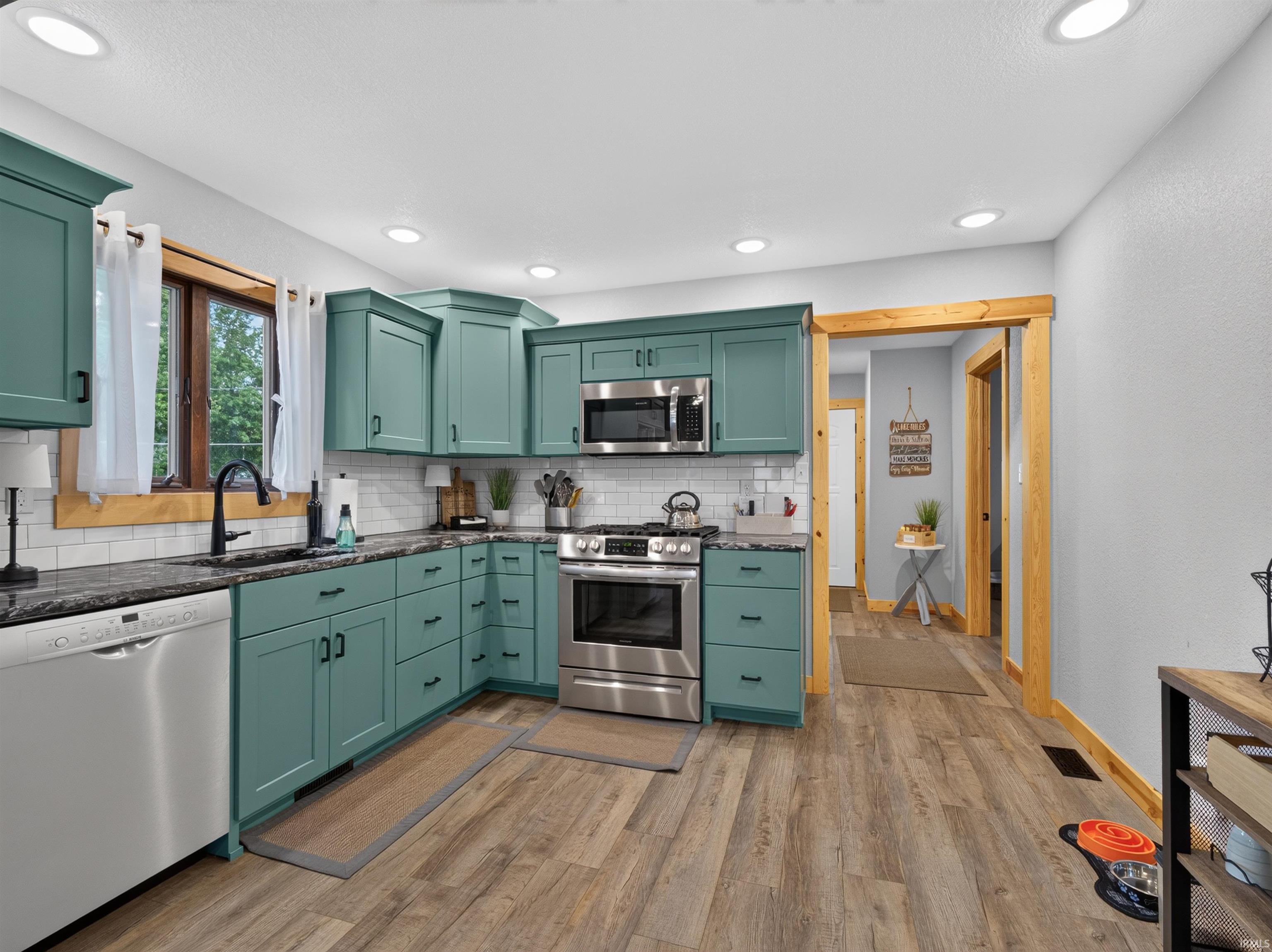Kitchen featuring abundant teal cabinetry, dark countertops, a white subway tile backsplash, stainless steel appliances, and wood-finish flooring