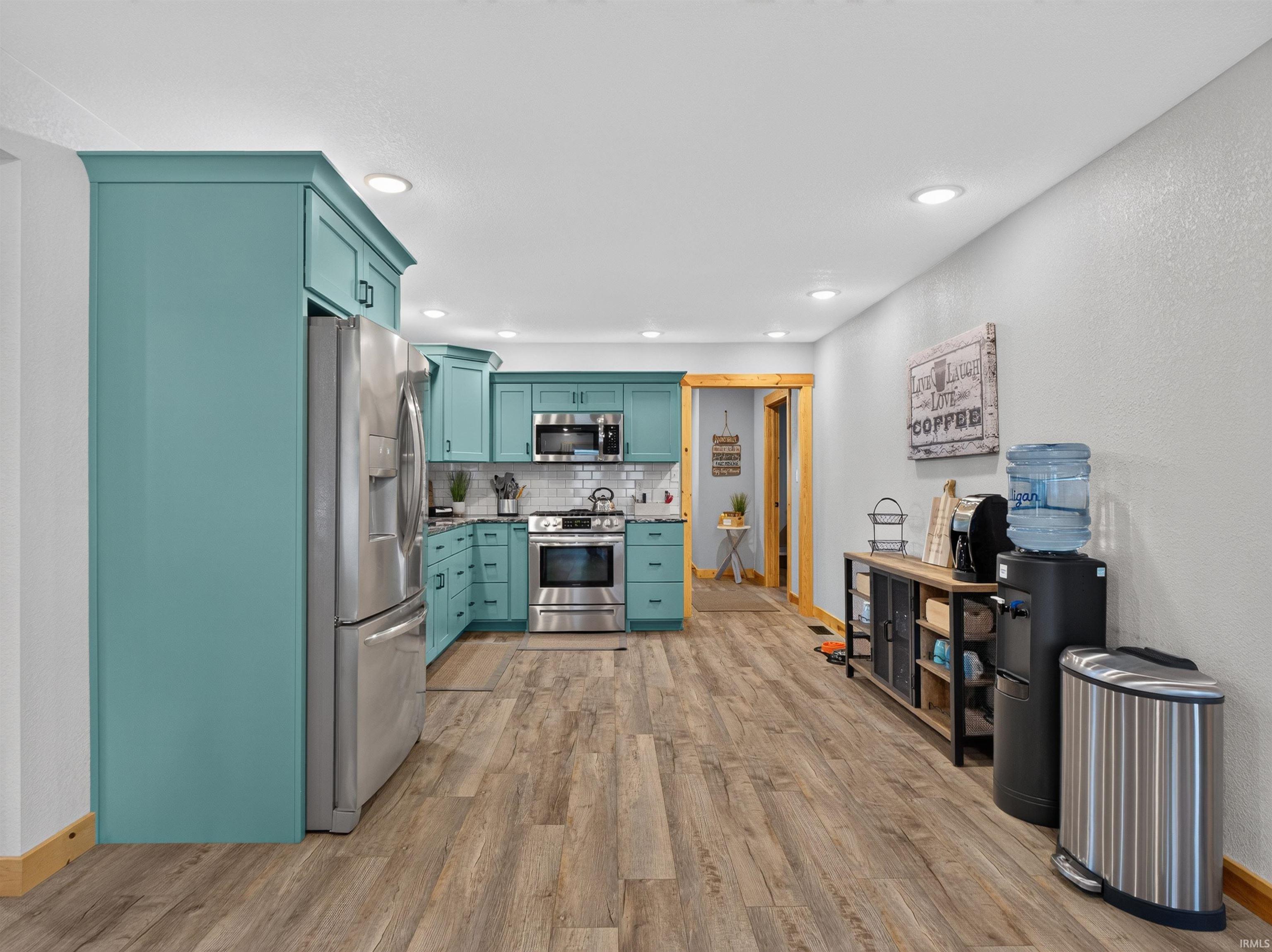 Kitchen featuring teal cabinetry, stainless steel appliances, wood-finish flooring, recessed lighting, and a white subway tile backsplash