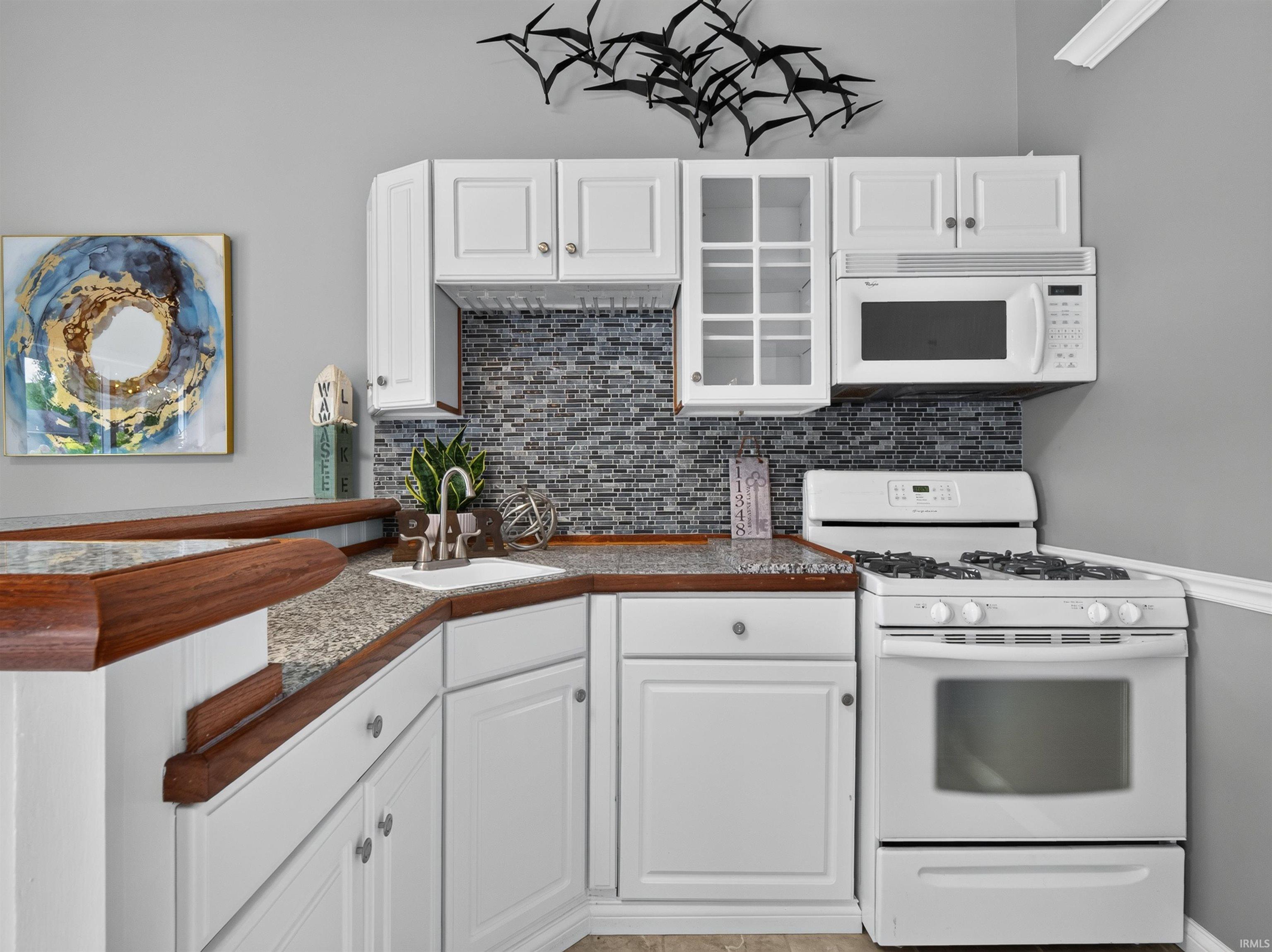 Compact kitchen featuring white cabinetry, granite-finish countertops, a mosaic tile backsplash, built-in microwave, and a gas range
