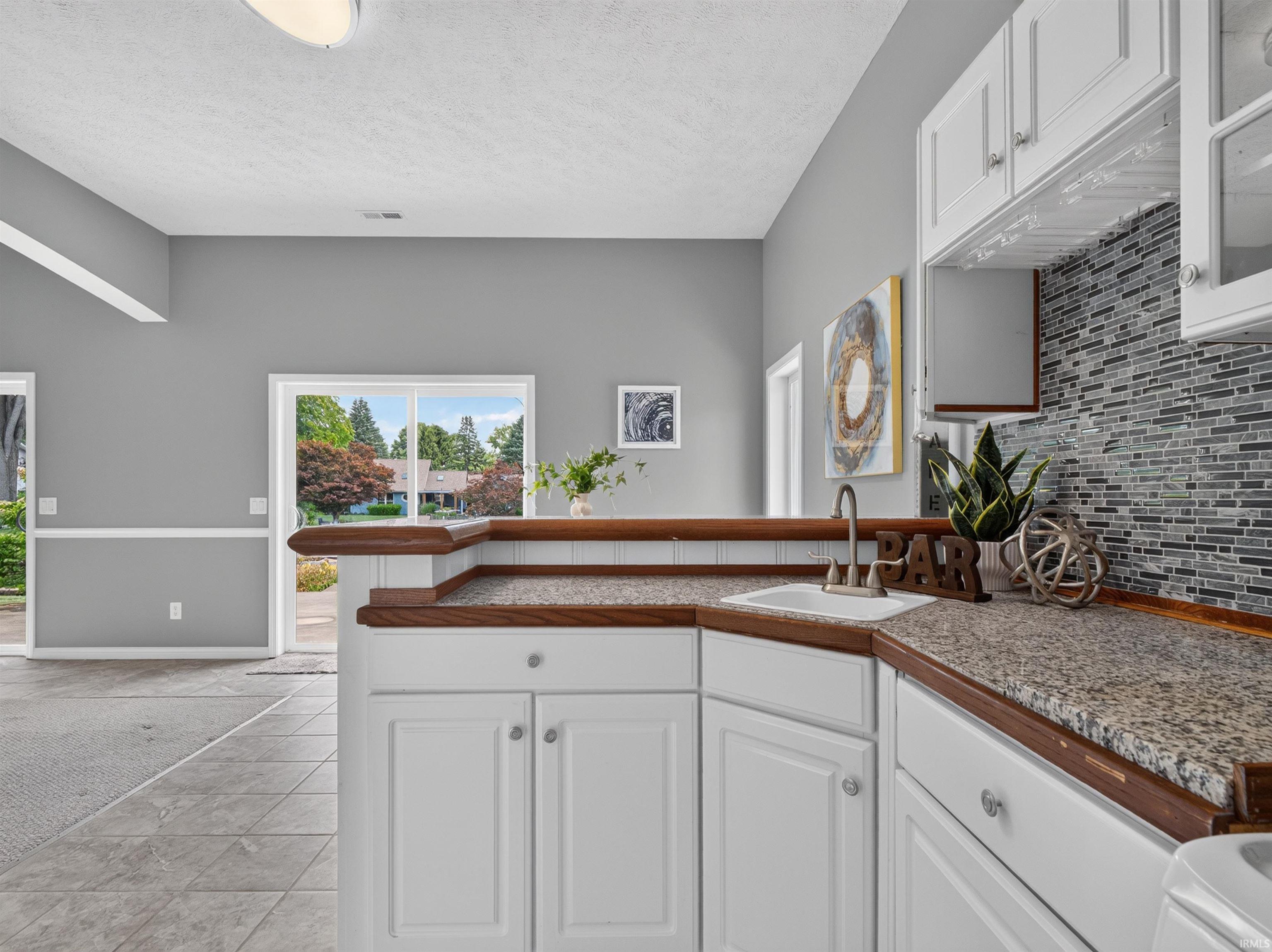 Wet bar featuring white cabinetry, granite countertops, an undermount sink, and a glass tile backsplash