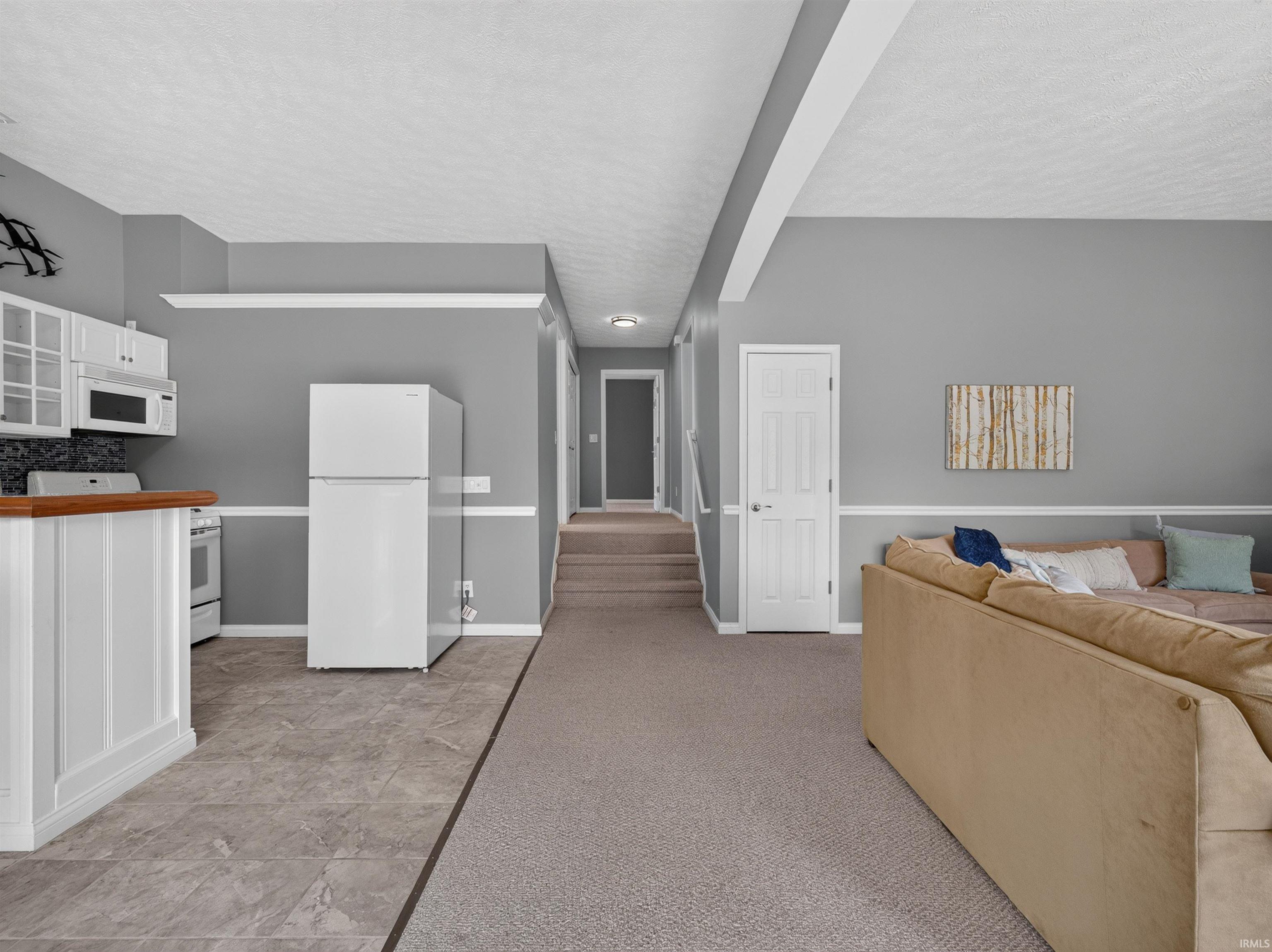 Lower-level living area with an integrated kitchenette featuring white cabinetry, a wood-finish countertop, and a tile backsplash