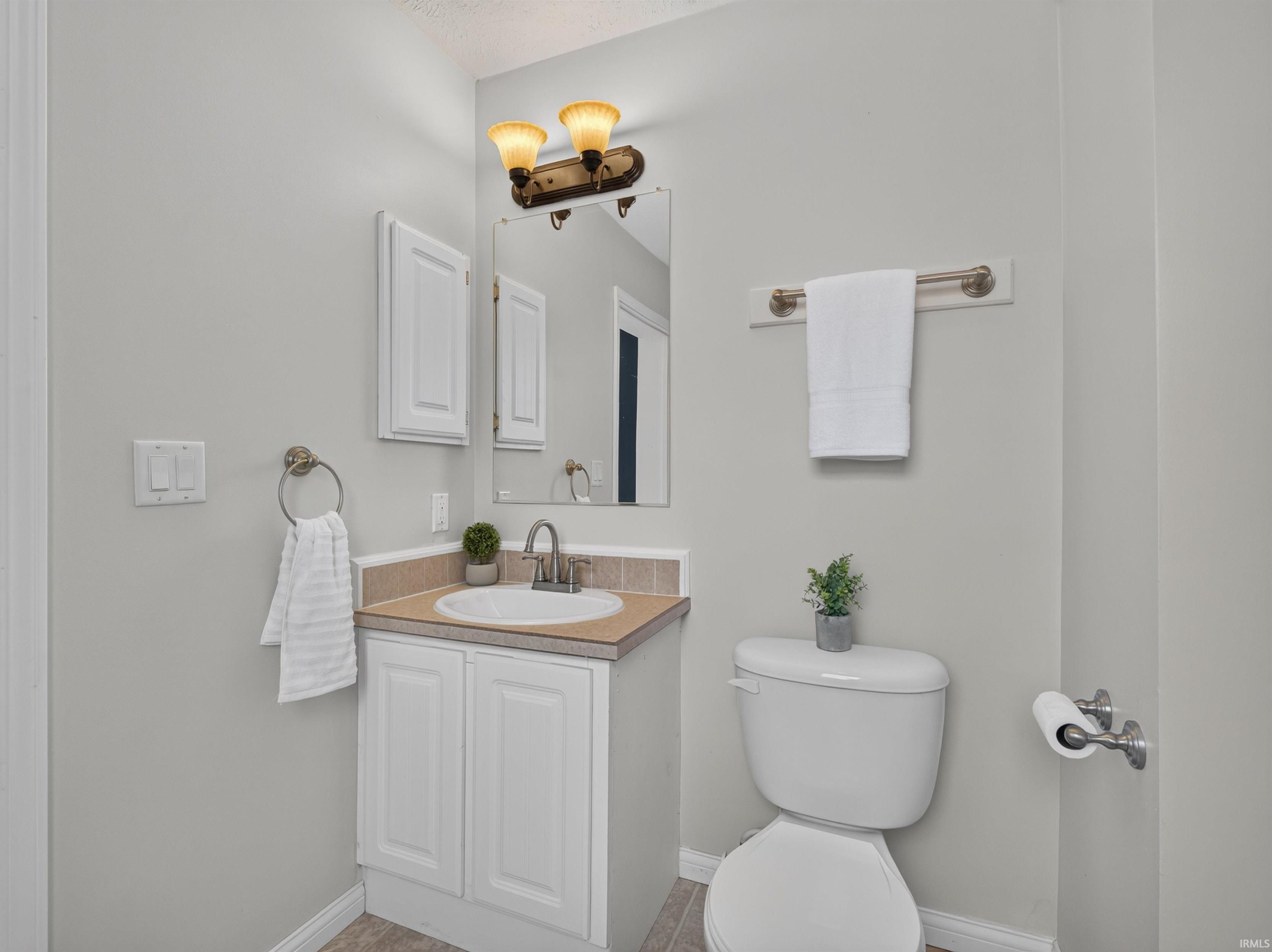 Bathroom featuring a white vanity with a tan countertop, a white sink, and a dual-bulb wall sconce