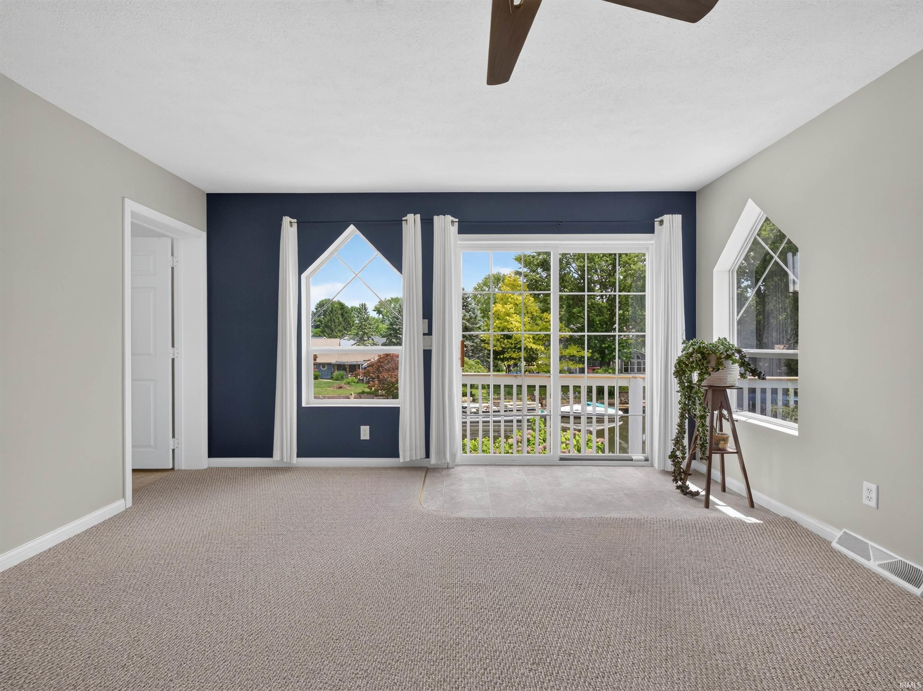 Spacious interior featuring a sliding glass door, two large arched windows, light-toned carpeting, and a ceiling fan