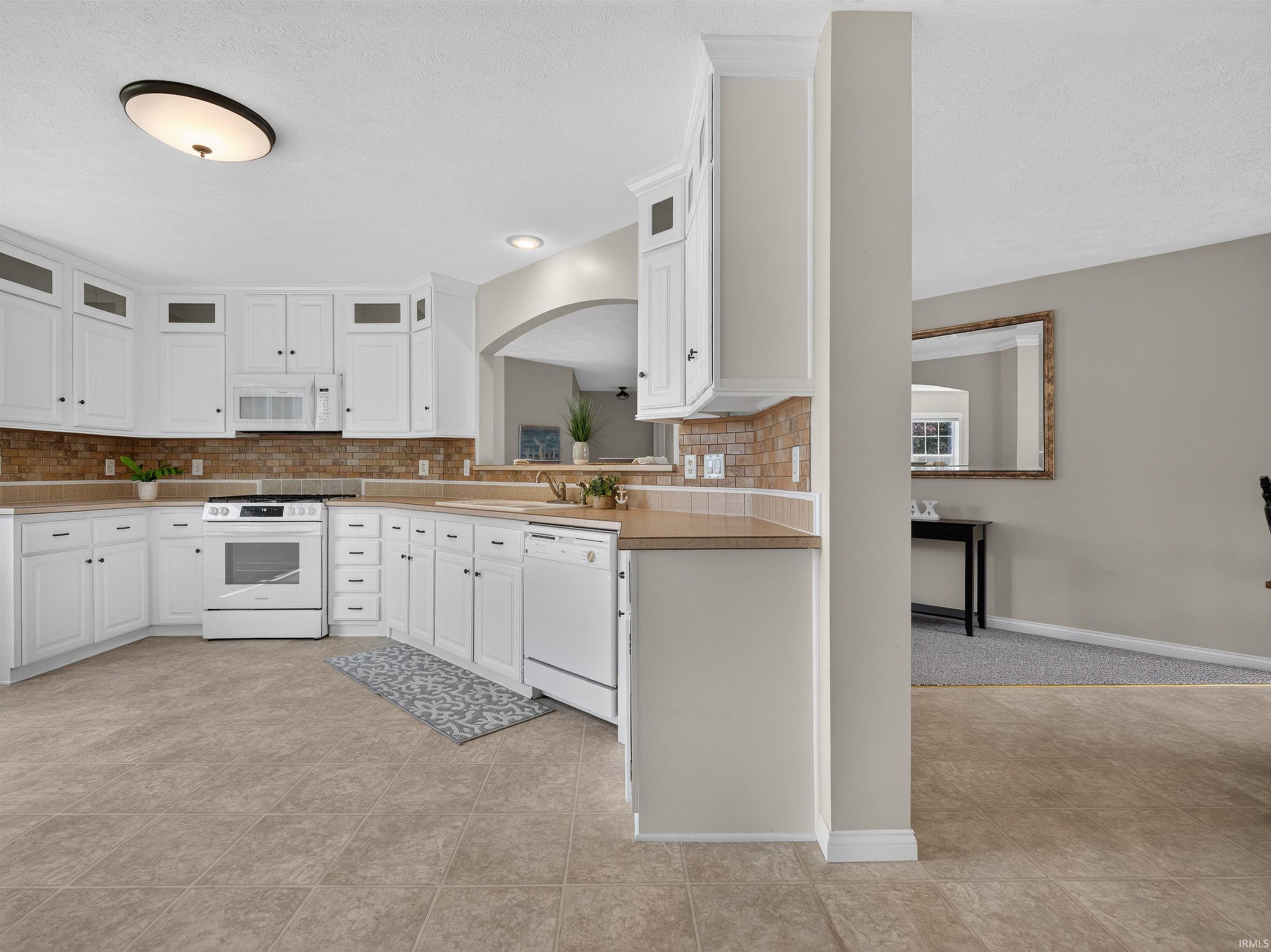 U-shaped kitchen featuring white cabinetry, light-toned countertops, and a brick-patterned backsplash