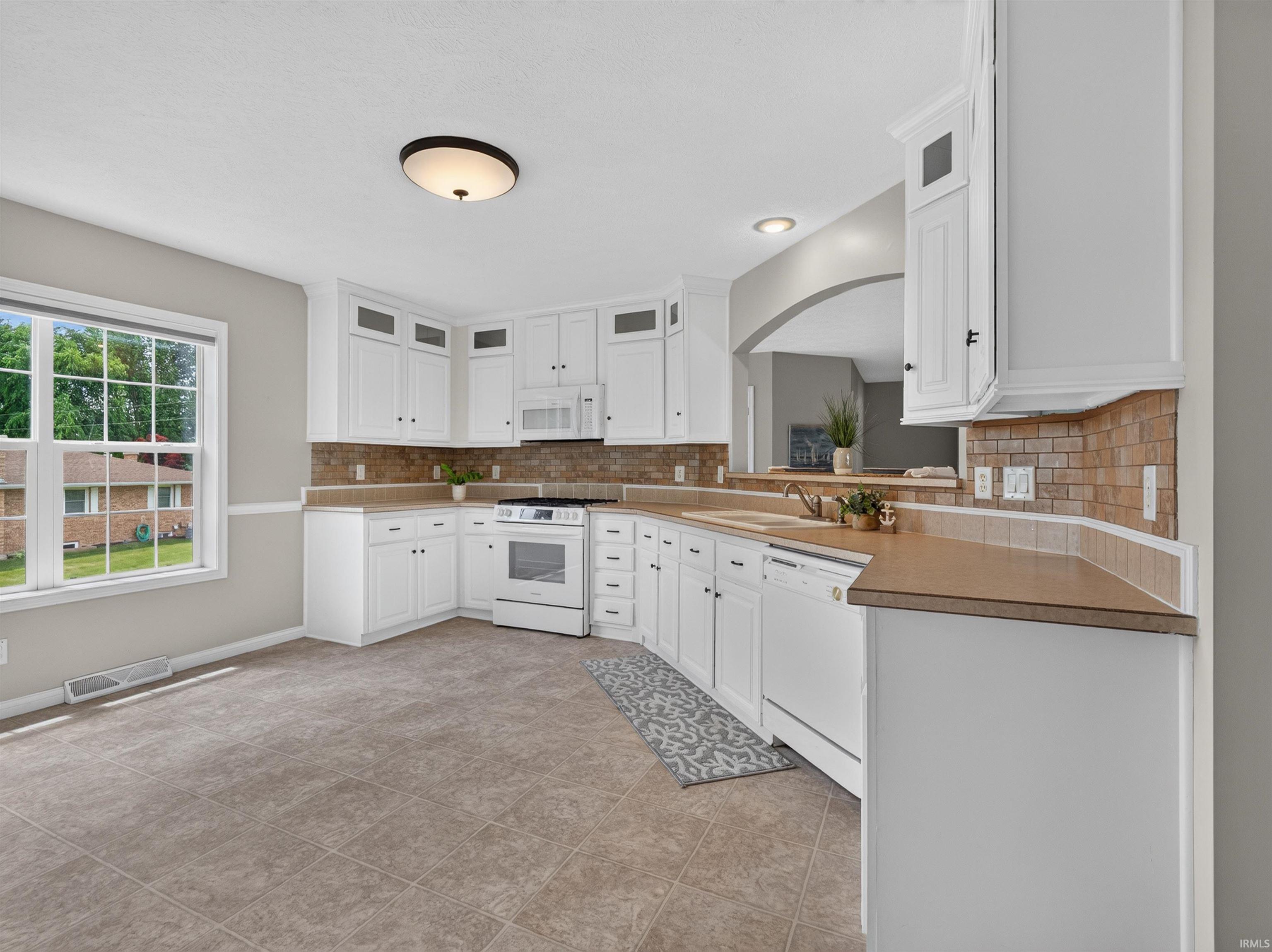 Well-appointed kitchen featuring white cabinetry with dark hardware, a tile backsplash, and a white appliance suite