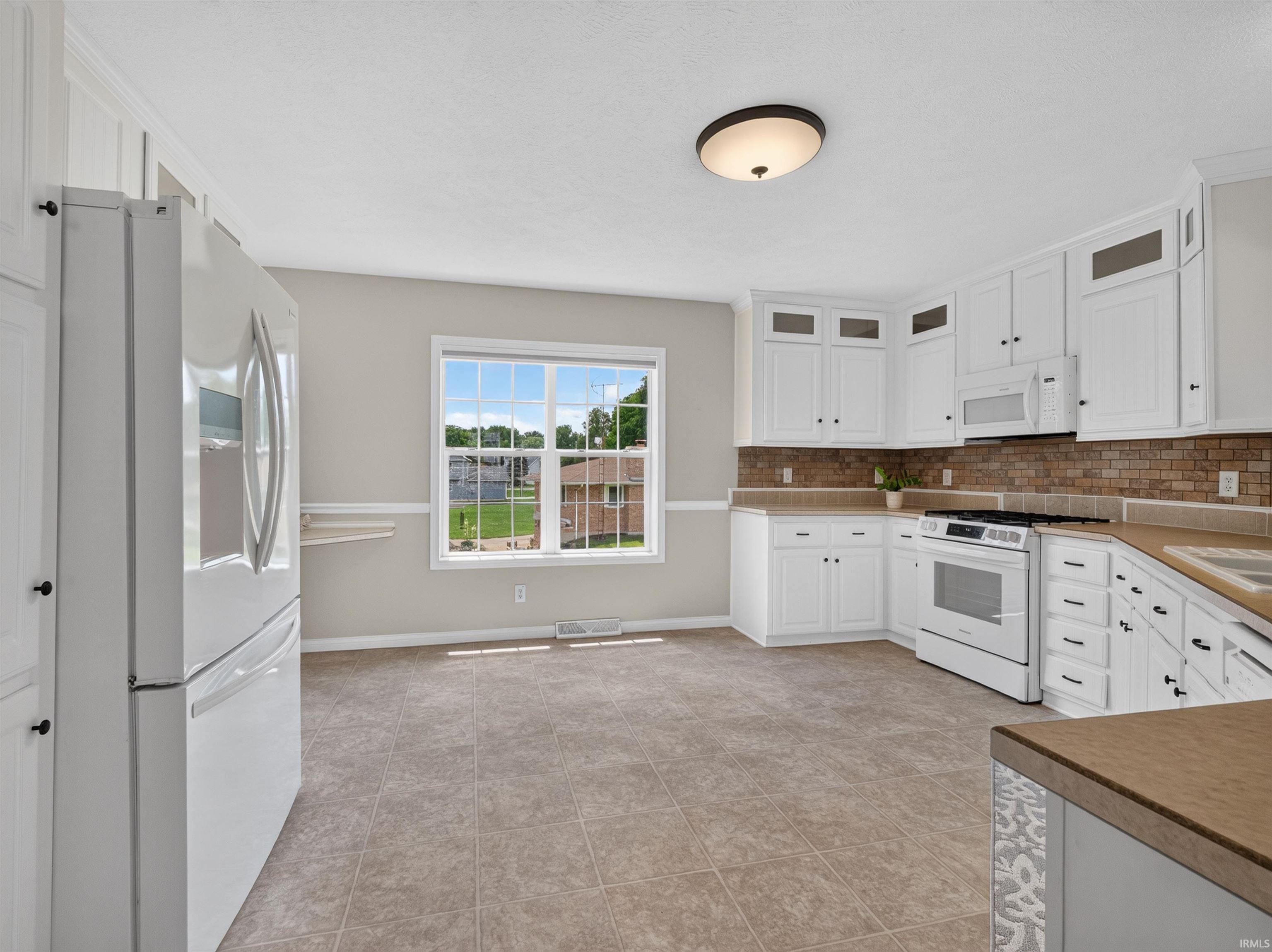 Open-concept kitchen featuring white cabinetry, a white appliance suite, and a brown tiled backsplash