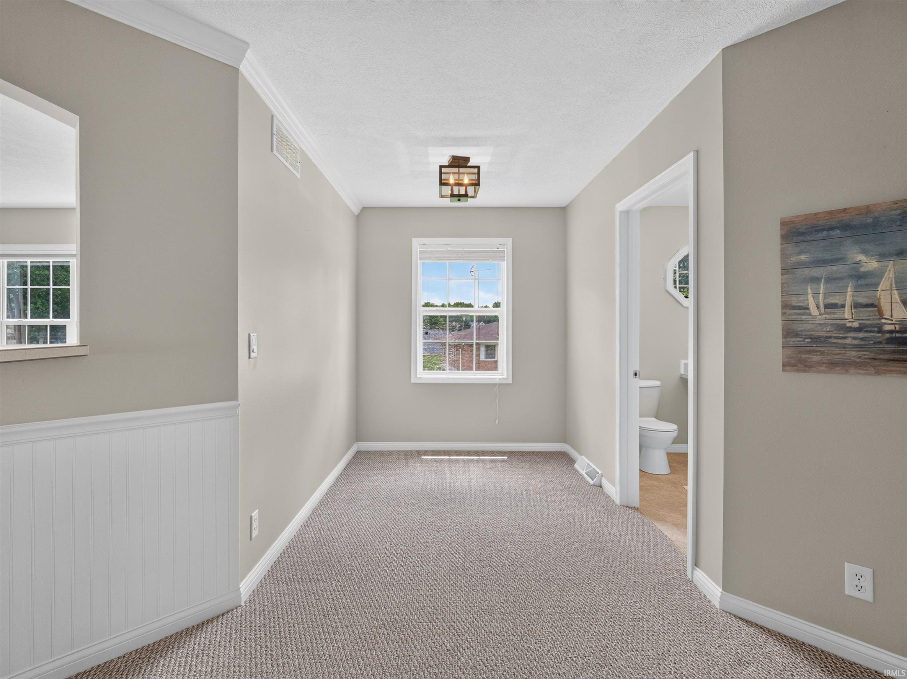 Carpeted hallway featuring a window with natural light, crown molding, and wainscoting detail