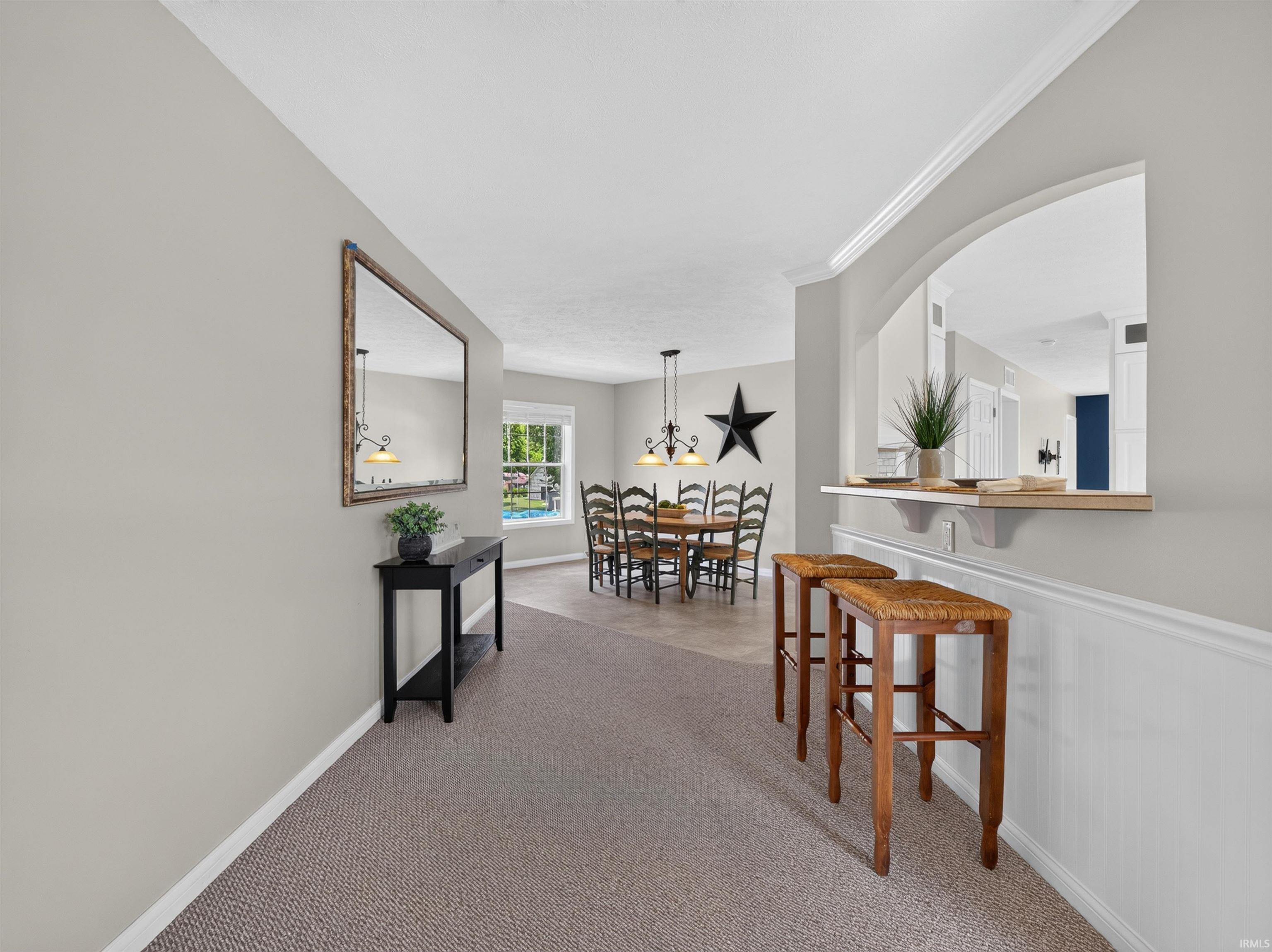 Carpeted entryway with a decorative mirror and console table, opening to a dining area