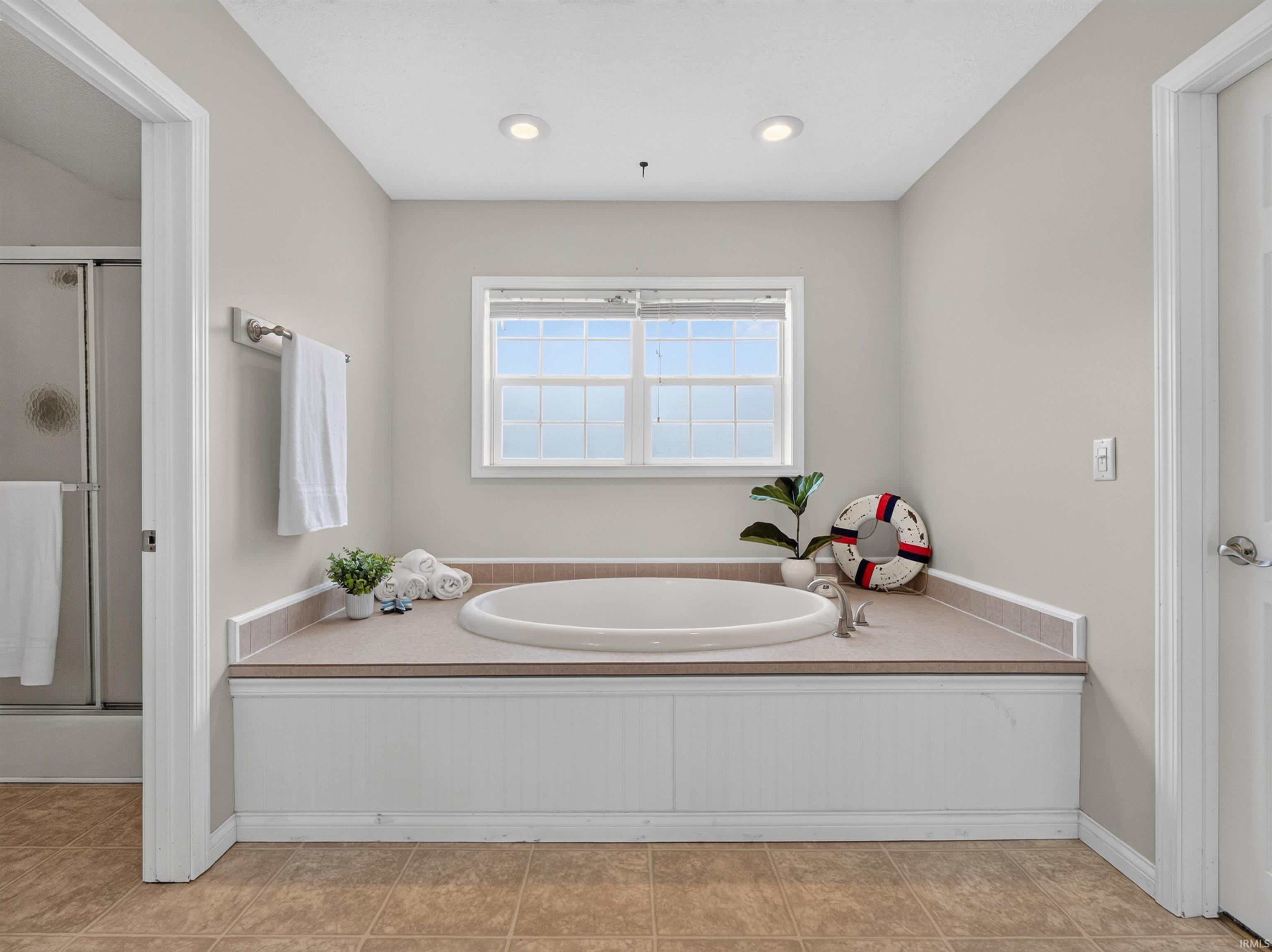 Soaking tub with a tiled surround, recessed lighting, and a multi-pane window