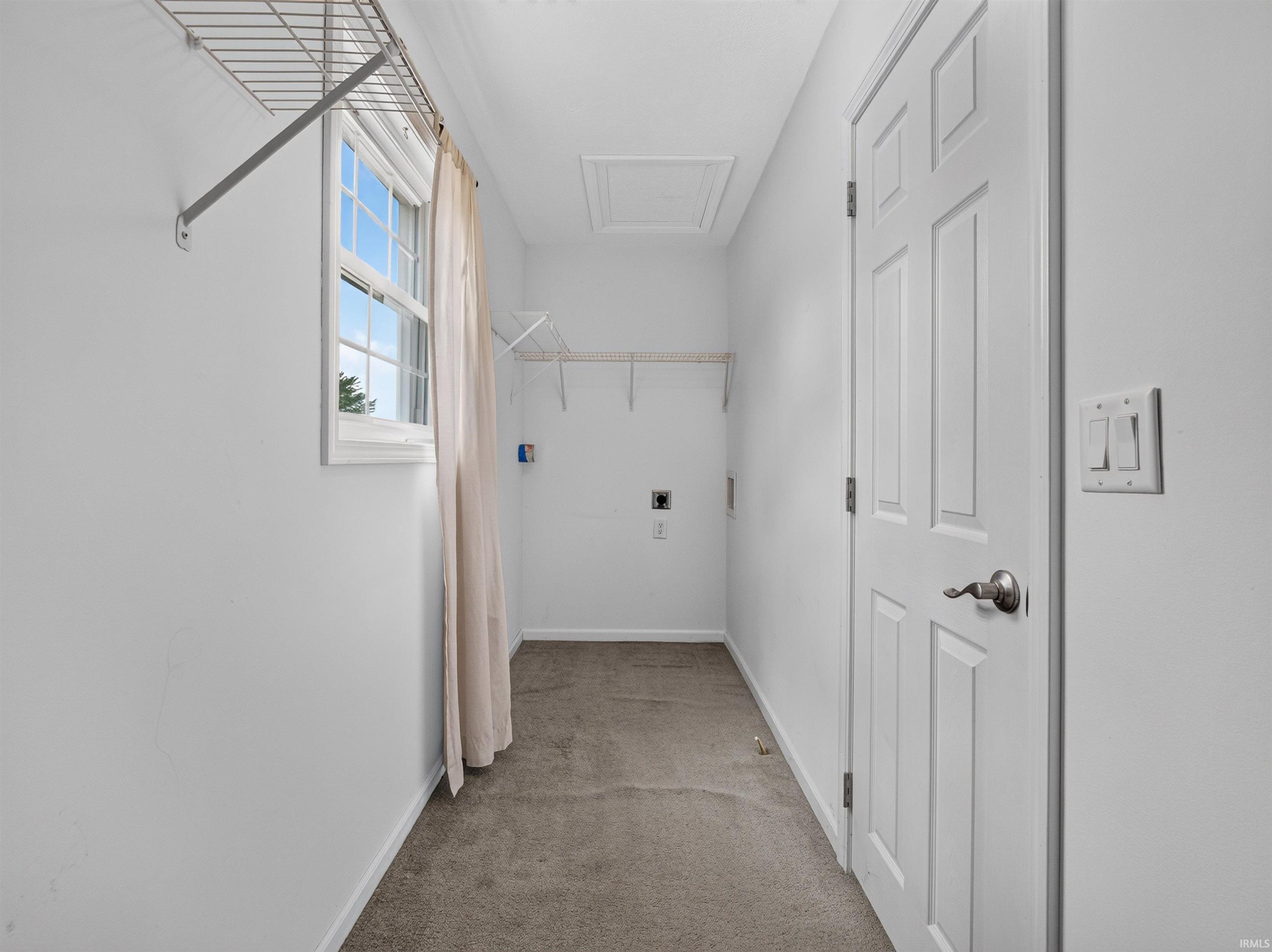 Dedicated laundry room with a window, white paneled door, wall-mounted shelving, and carpeted flooring