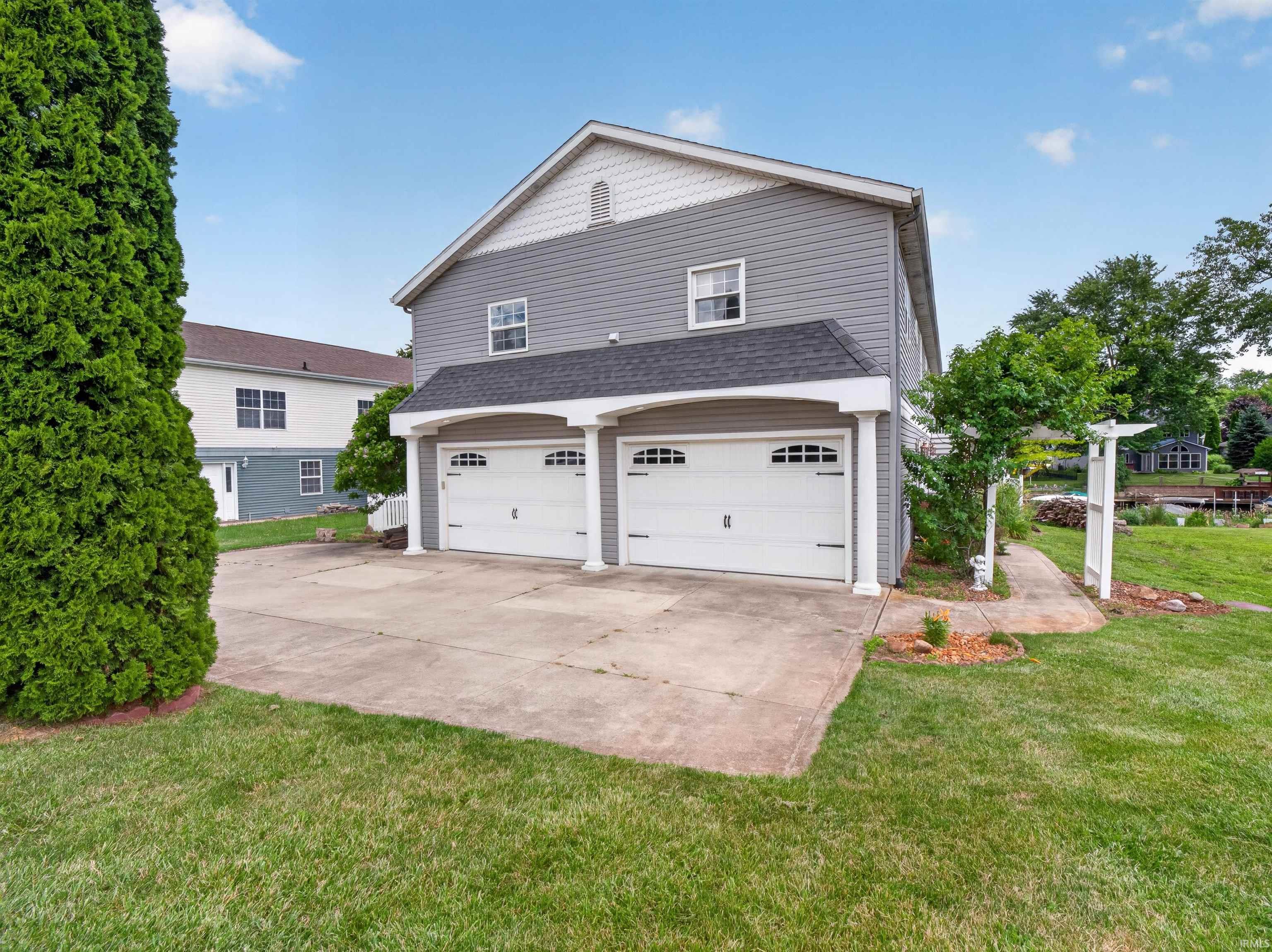 Two-story exterior with gray siding, featuring a dual garage with arched window inserts, a concrete driveway, and a front gabled roofline
