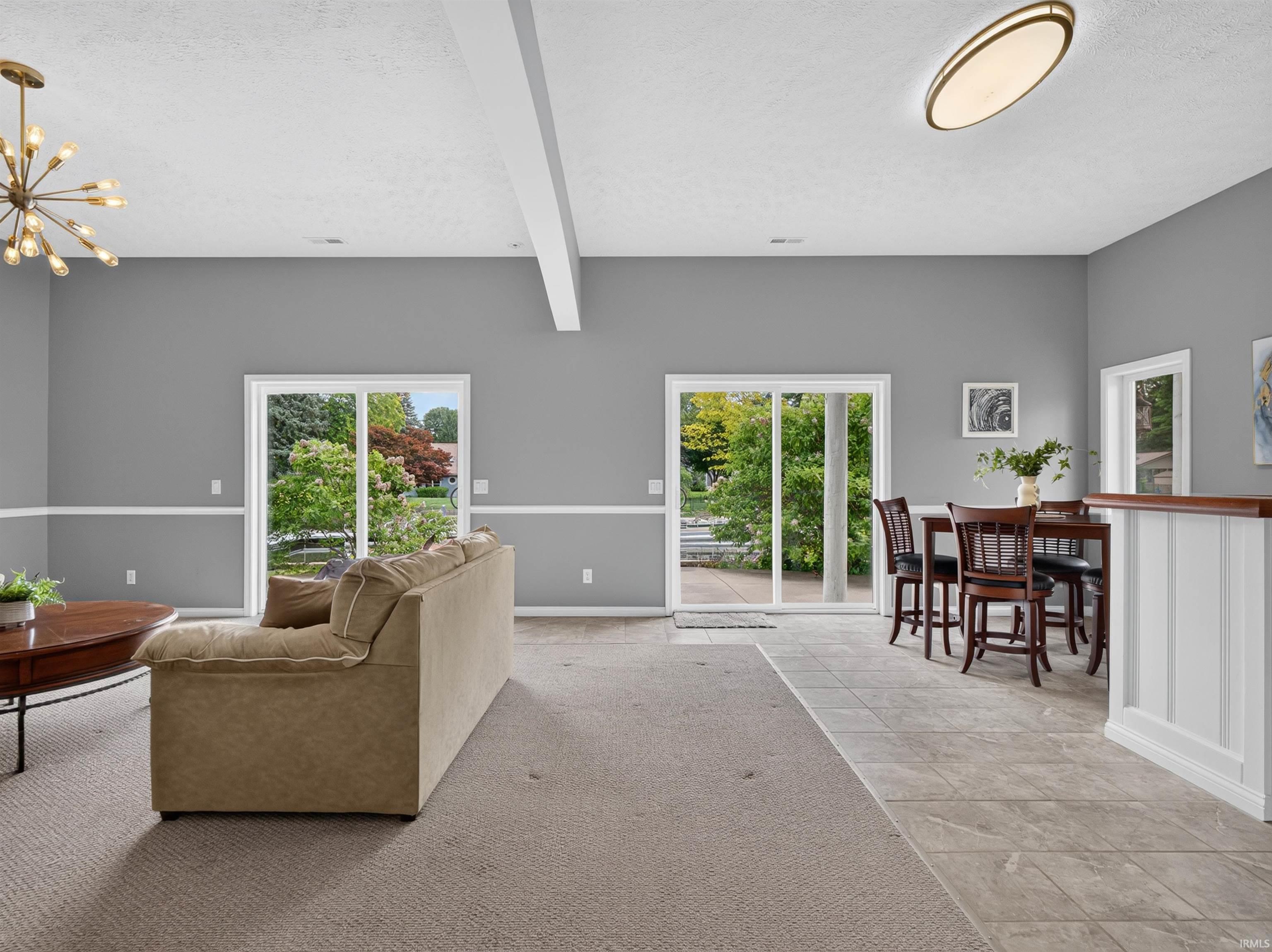 Spacious open-concept room featuring a vaulted ceiling with exposed beam, multiple sliding glass doors to the exterior, and a built-in bar