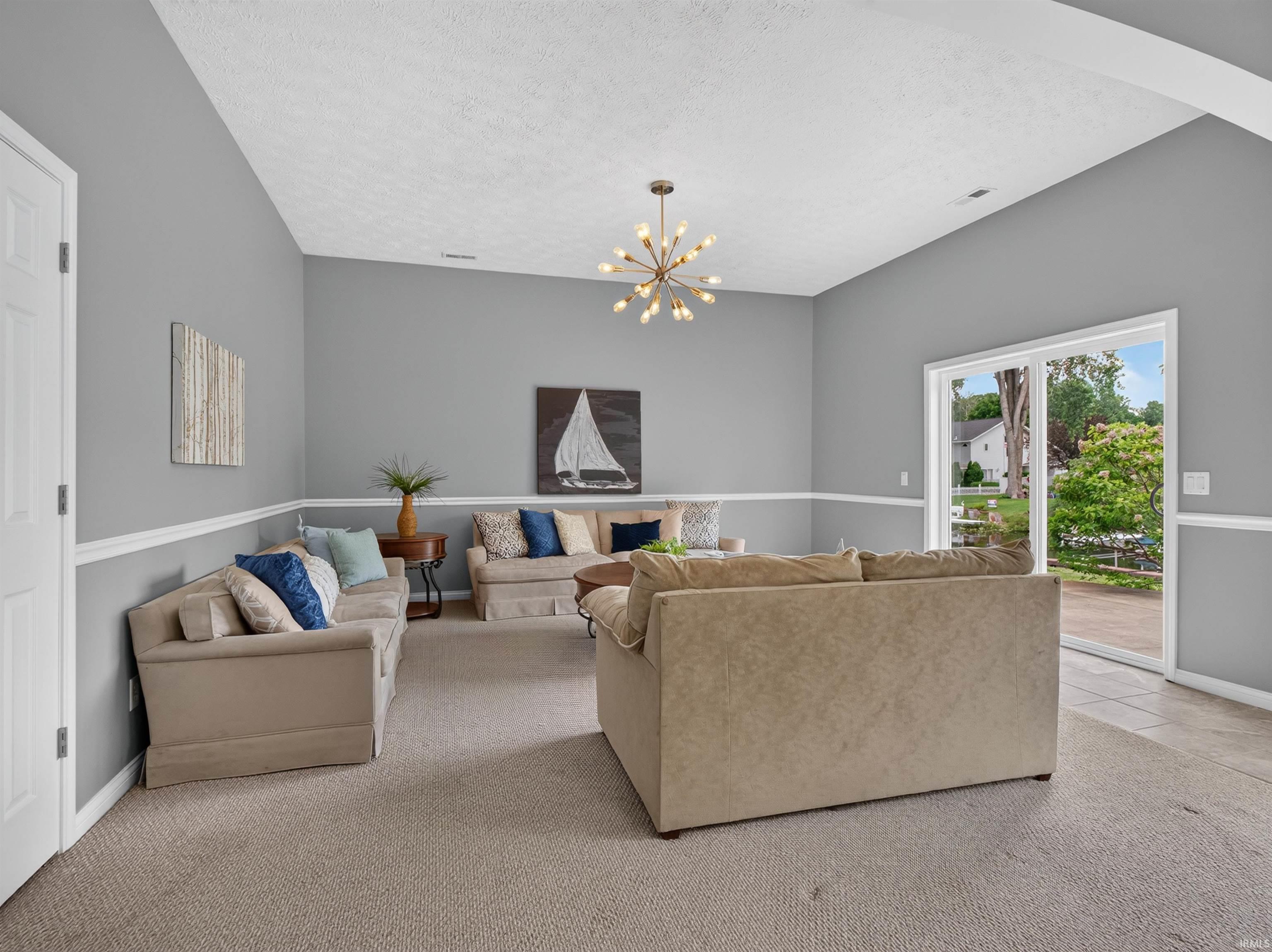 Spacious interior featuring a vaulted ceiling, a contemporary sputnik chandelier, and light gray wall paint with white chair rail molding