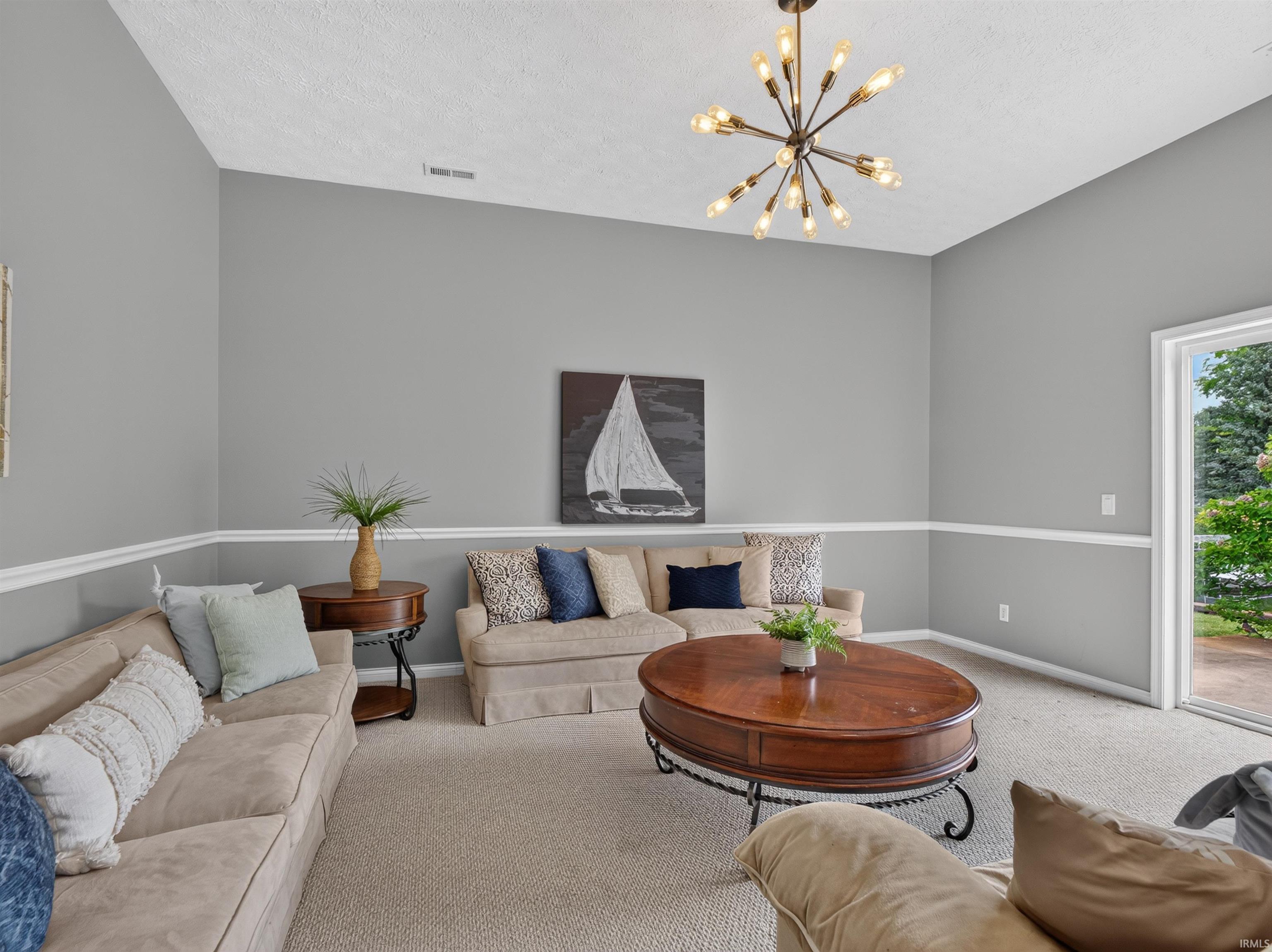 Spacious living area featuring a vaulted ceiling with a modern sputnik chandelier, light gray walls with chair rail molding, and neutral carpeting