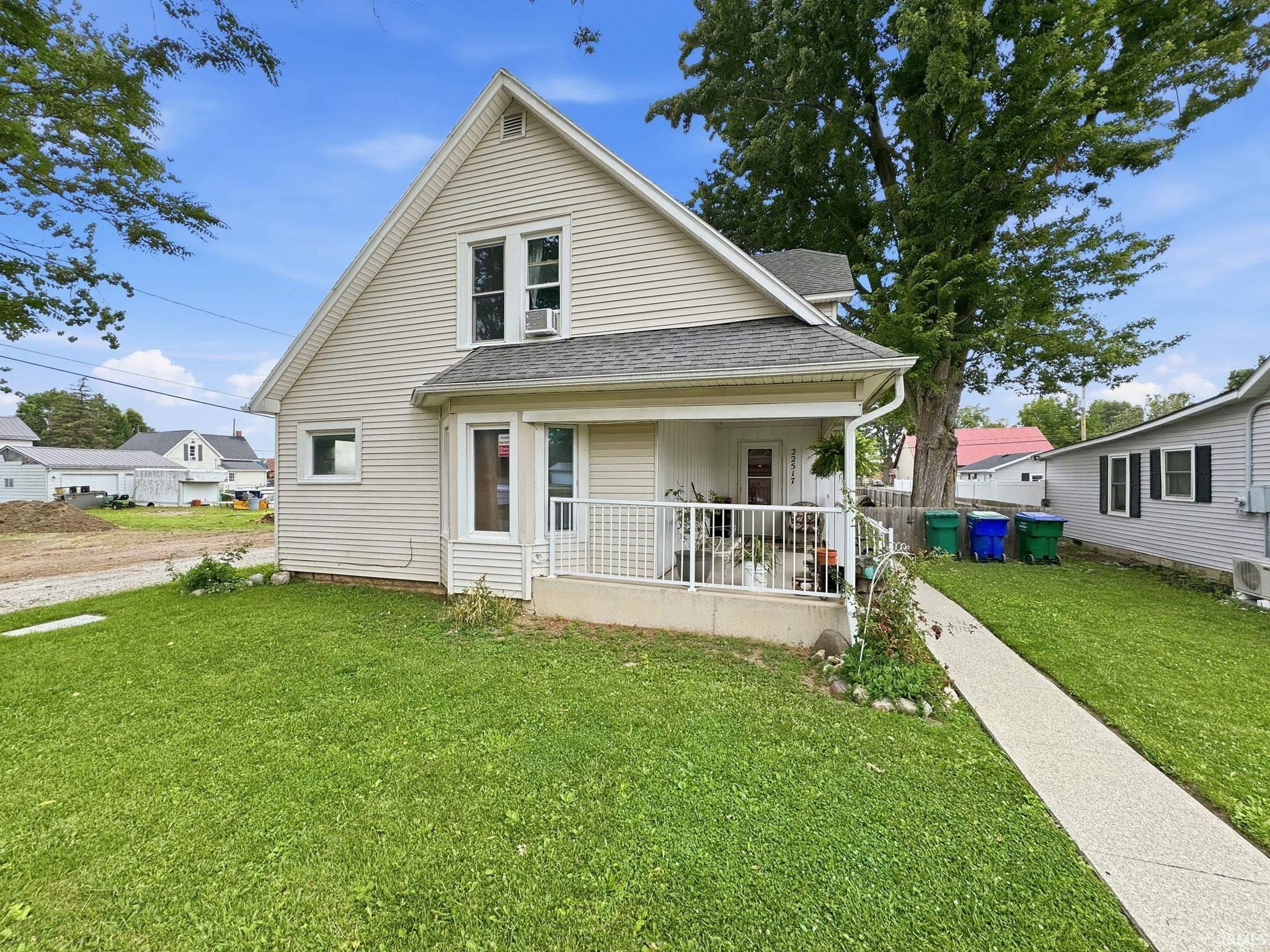 Siding exterior featuring a covered porch with white railings, a front lawn, and a concrete walkway