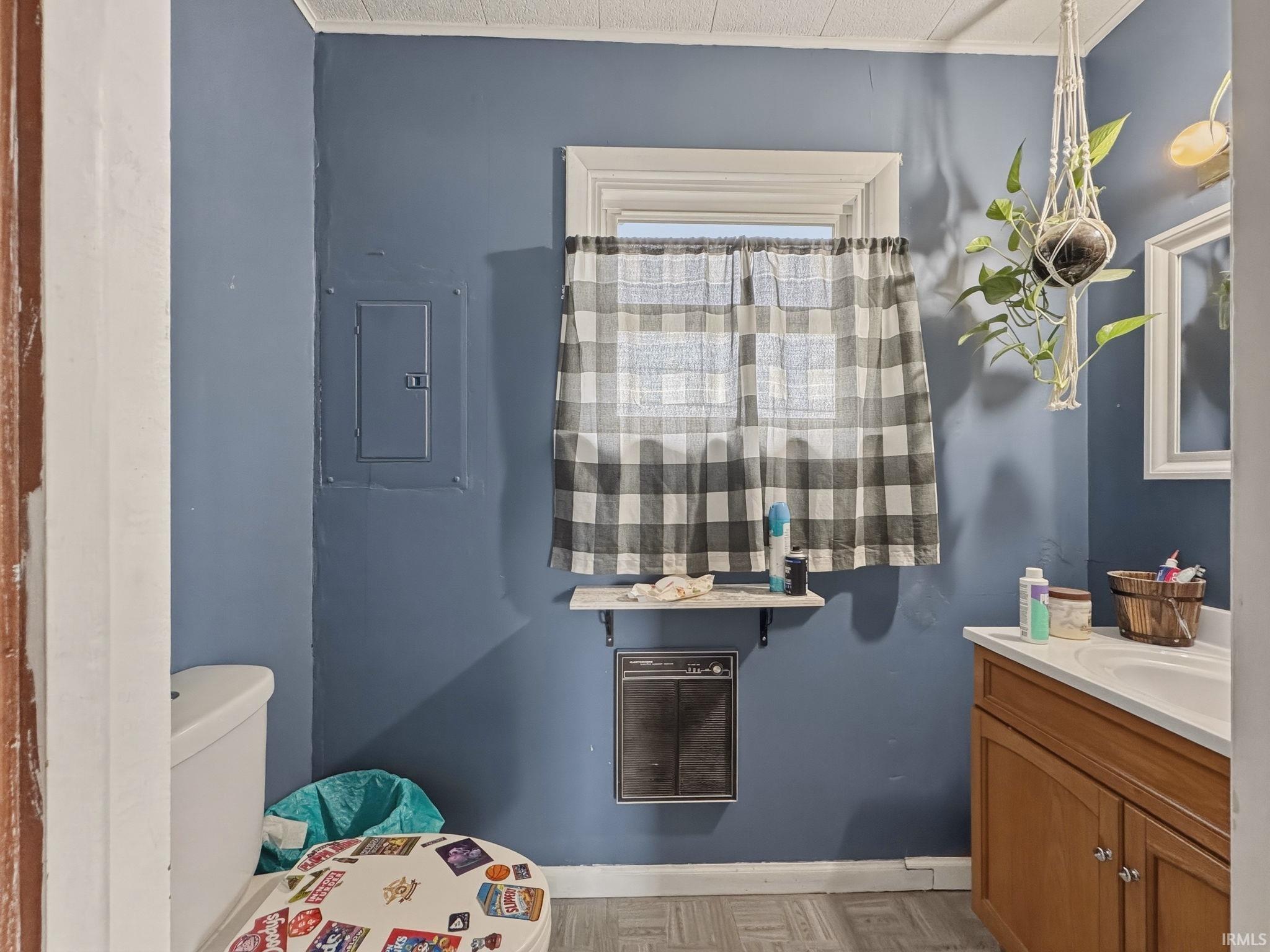 Bathroom featuring a white-framed window, a wood-finish vanity with an integrated sink, a wall-mounted heater, and light-toned flooring