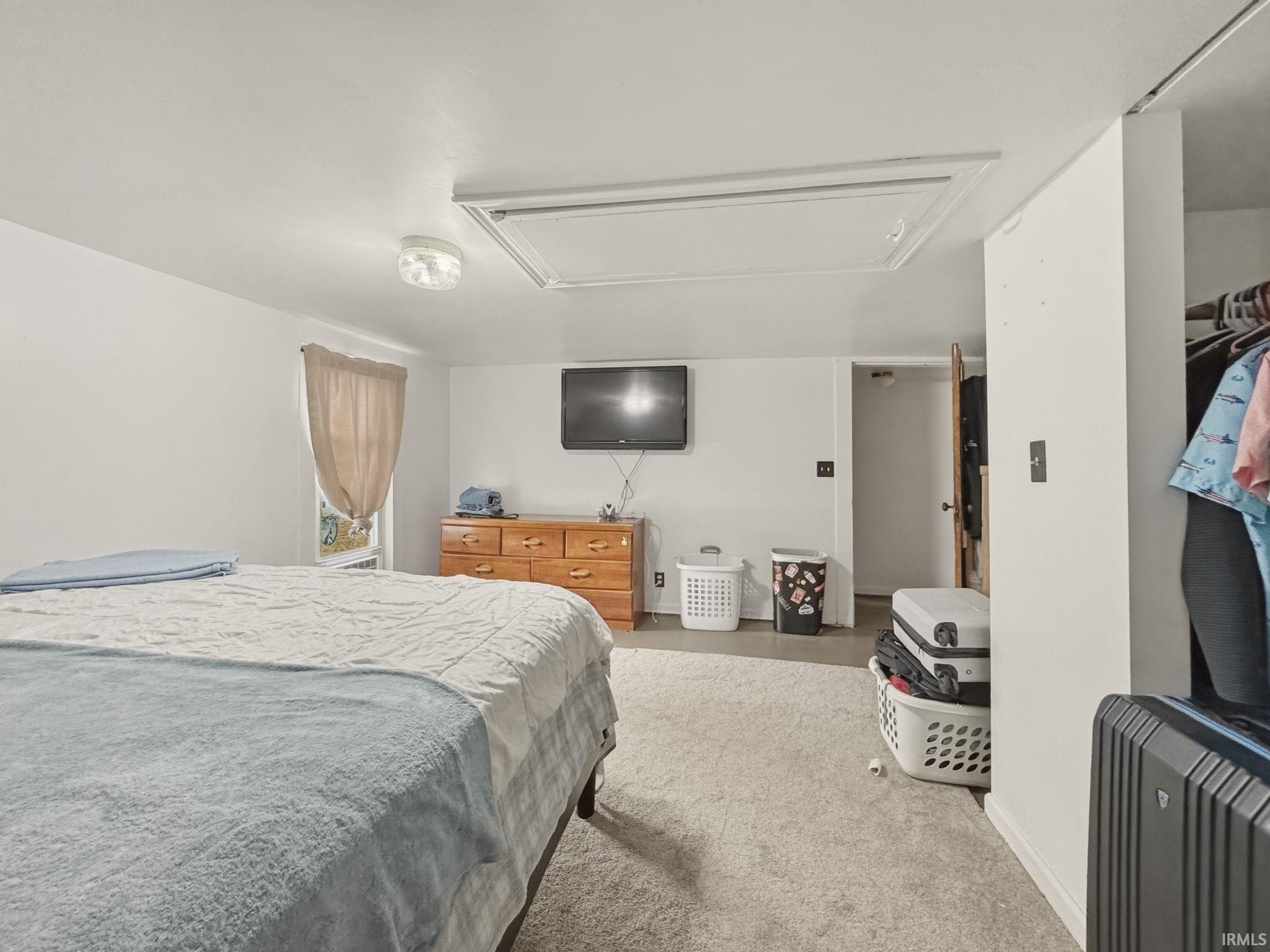 Carpeted room with a ceiling-mounted light fixture, a window with a fabric valence, and an attic access panel