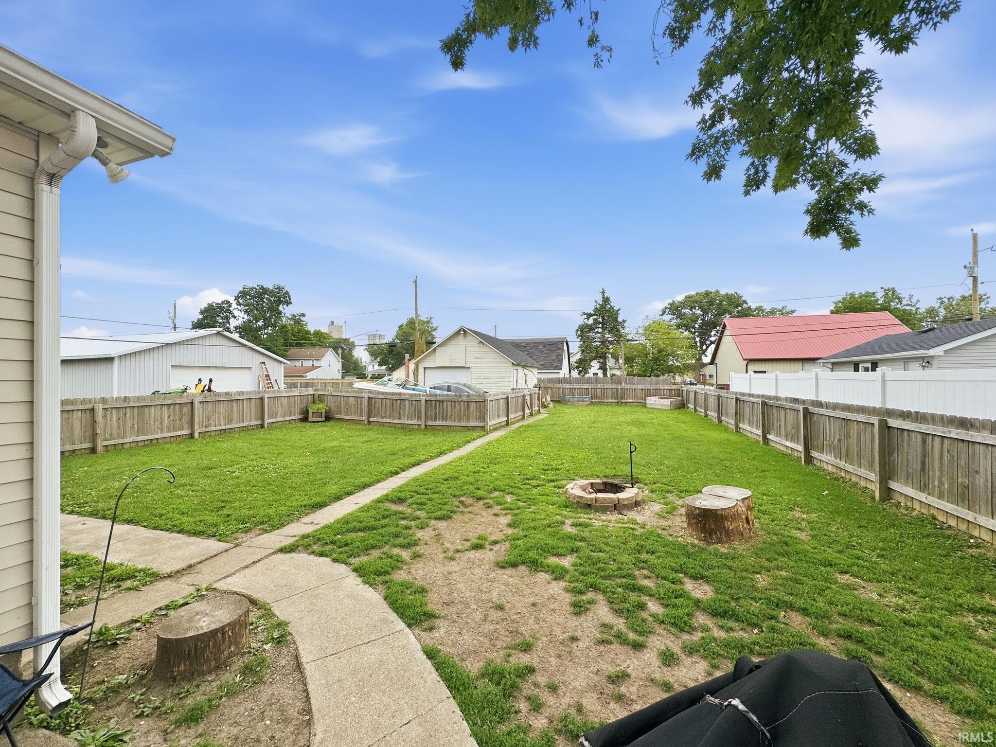 Expansive backyard featuring a partial privacy fence, concrete path, and a built-in fire pit