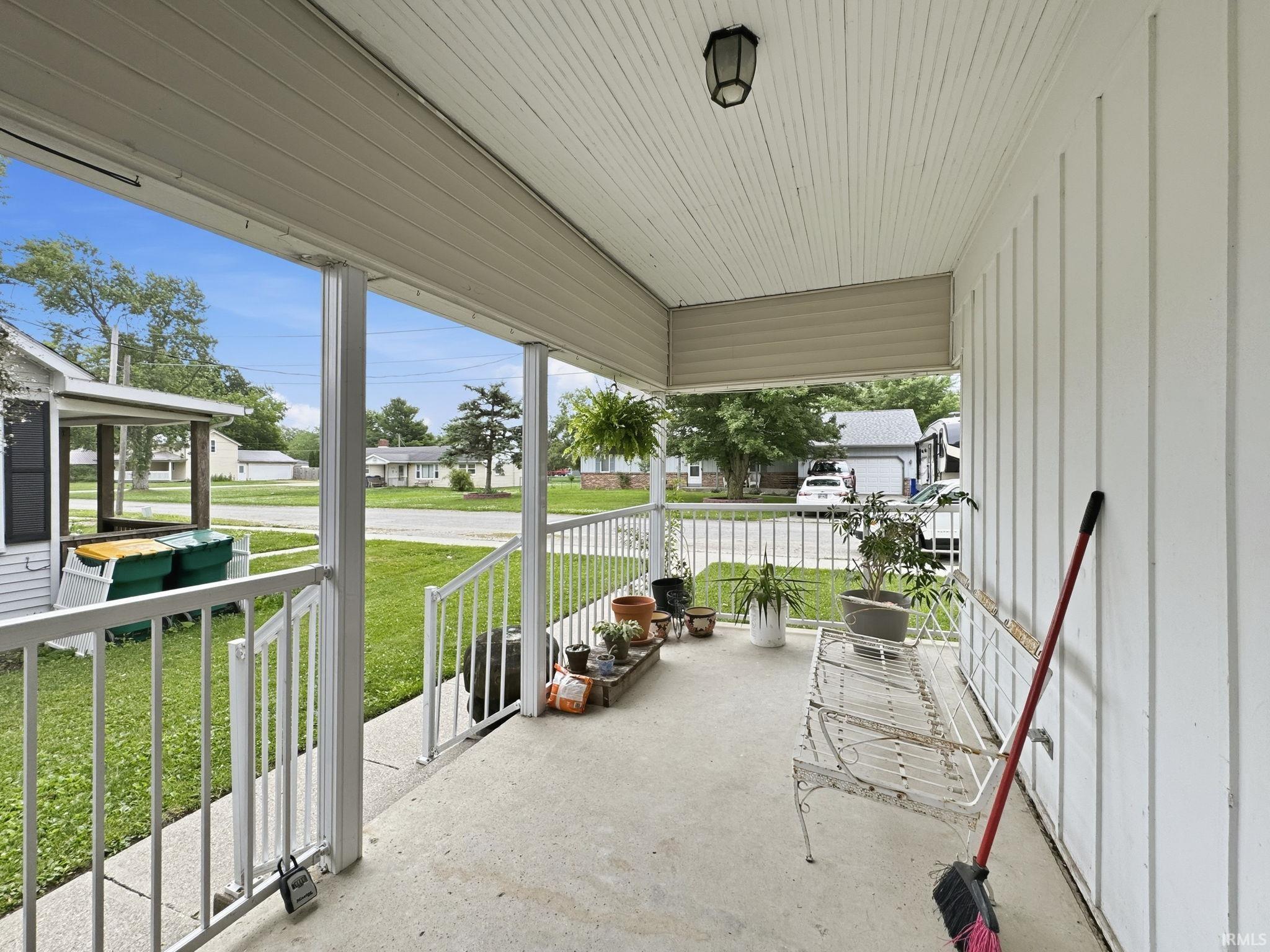 Covered front porch featuring a concrete floor, white vertical siding, white railing, and a beadboard ceiling with an attached light fixture
