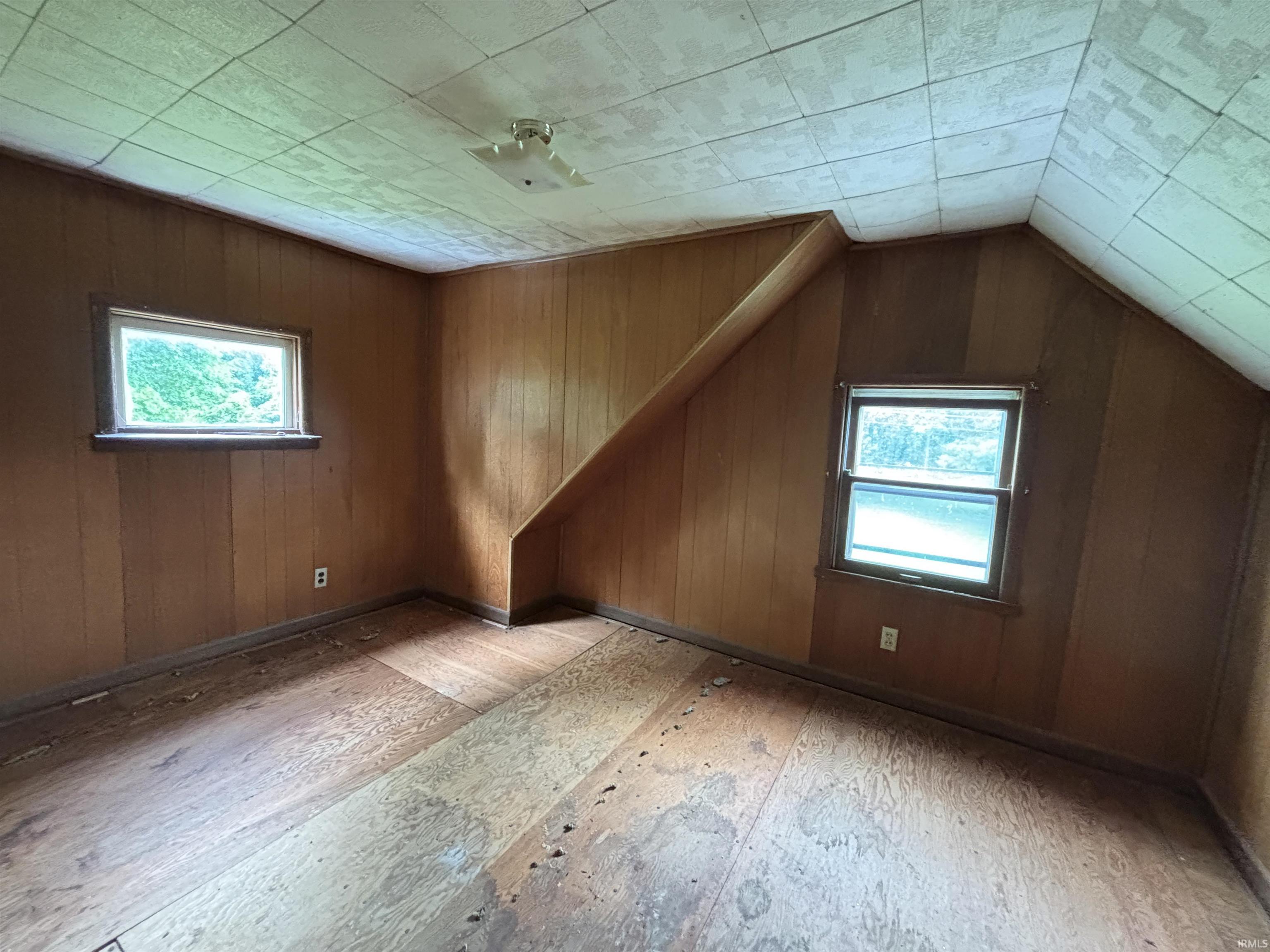 Room featuring wood paneling on walls, two windows providing natural light, and a sloped ceiling with acoustic tiles