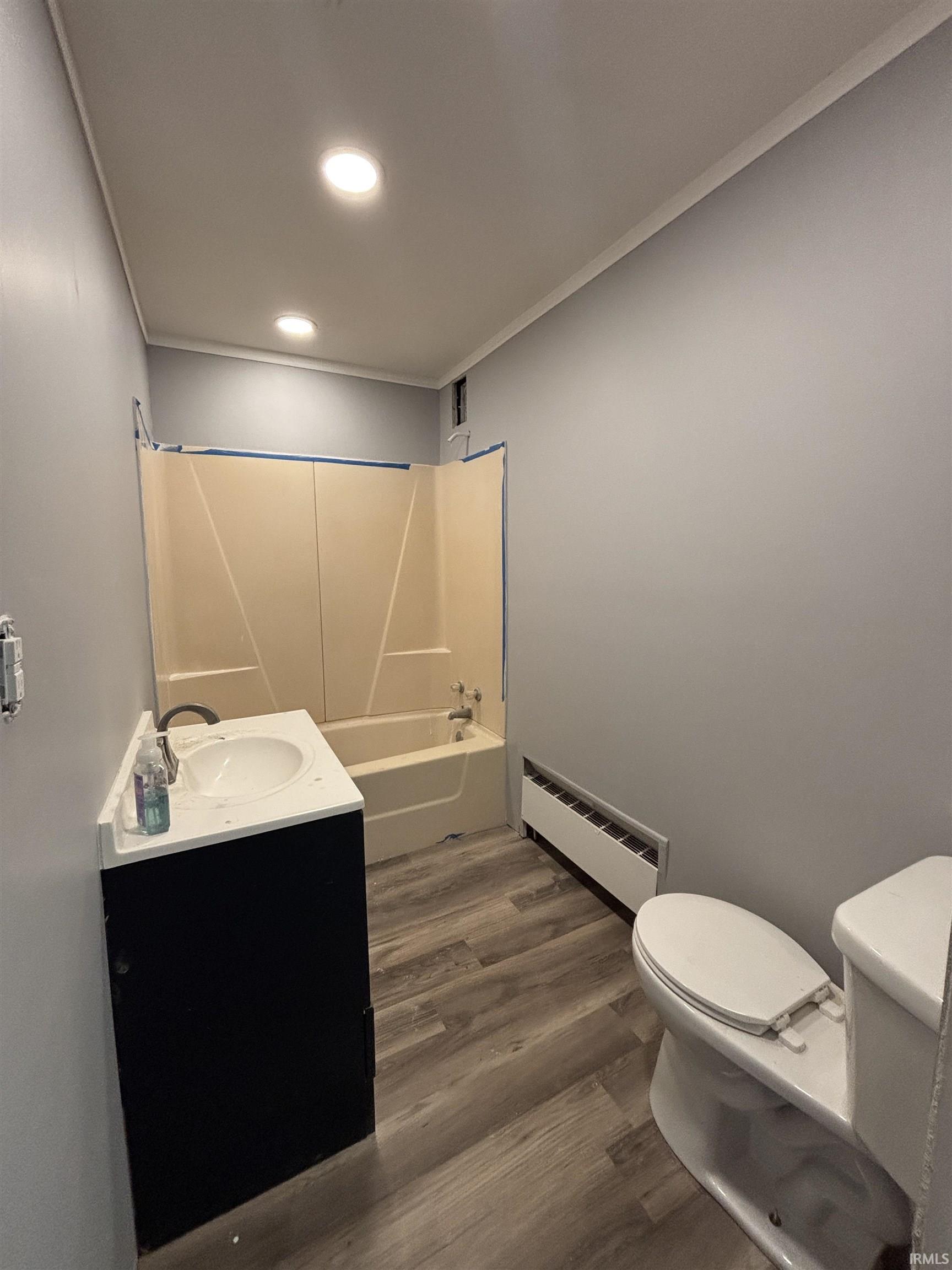 Bathroom featuring a vanity with an integrated sink, bathtub with shower surround, wood-finish flooring, and recessed ceiling lighting
