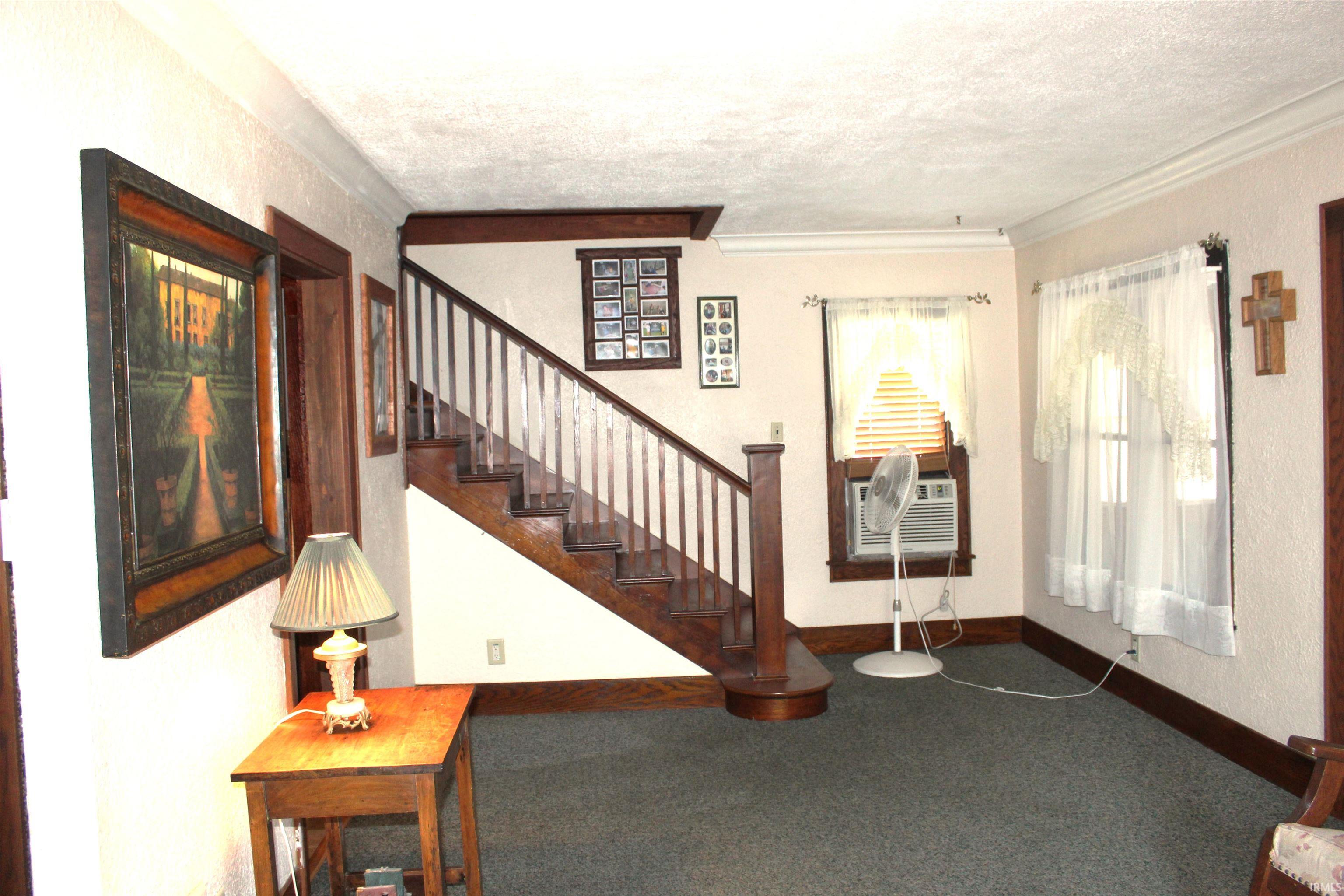Staircase with wood newel post and balusters, dark wood trim, wall-to-wall carpeting, and crown molding