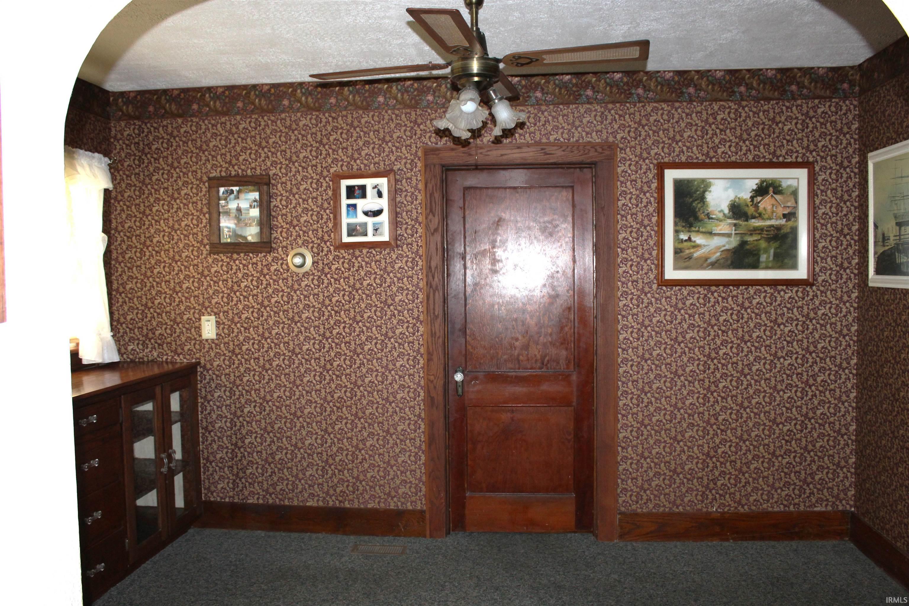 Interior room featuring patterned wallpaper, a wood-paneled door, and a ceiling fan with light fixture