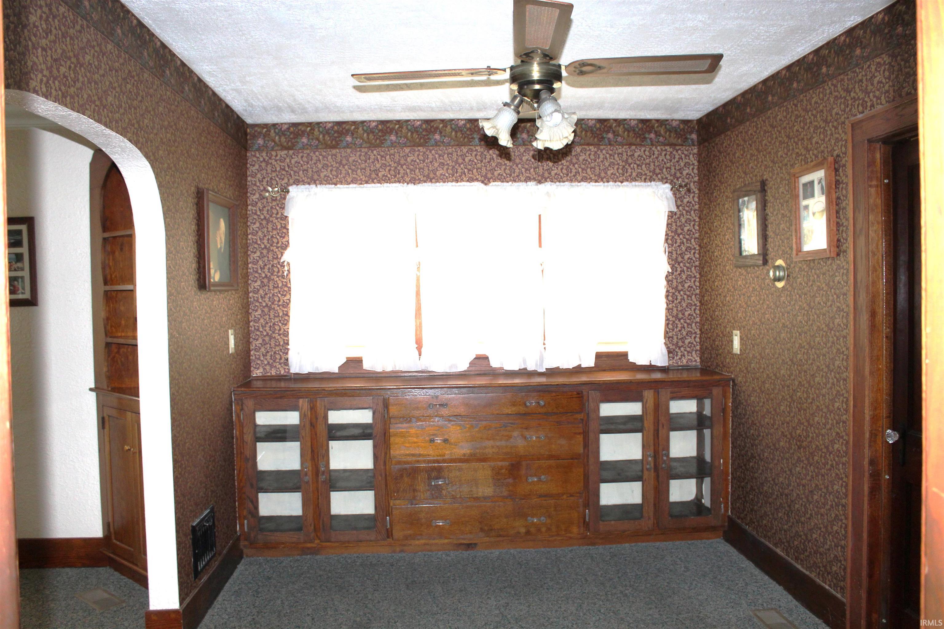 Built-in wooden cabinetry with glass-front doors, an arched doorway, and patterned wallpaper
