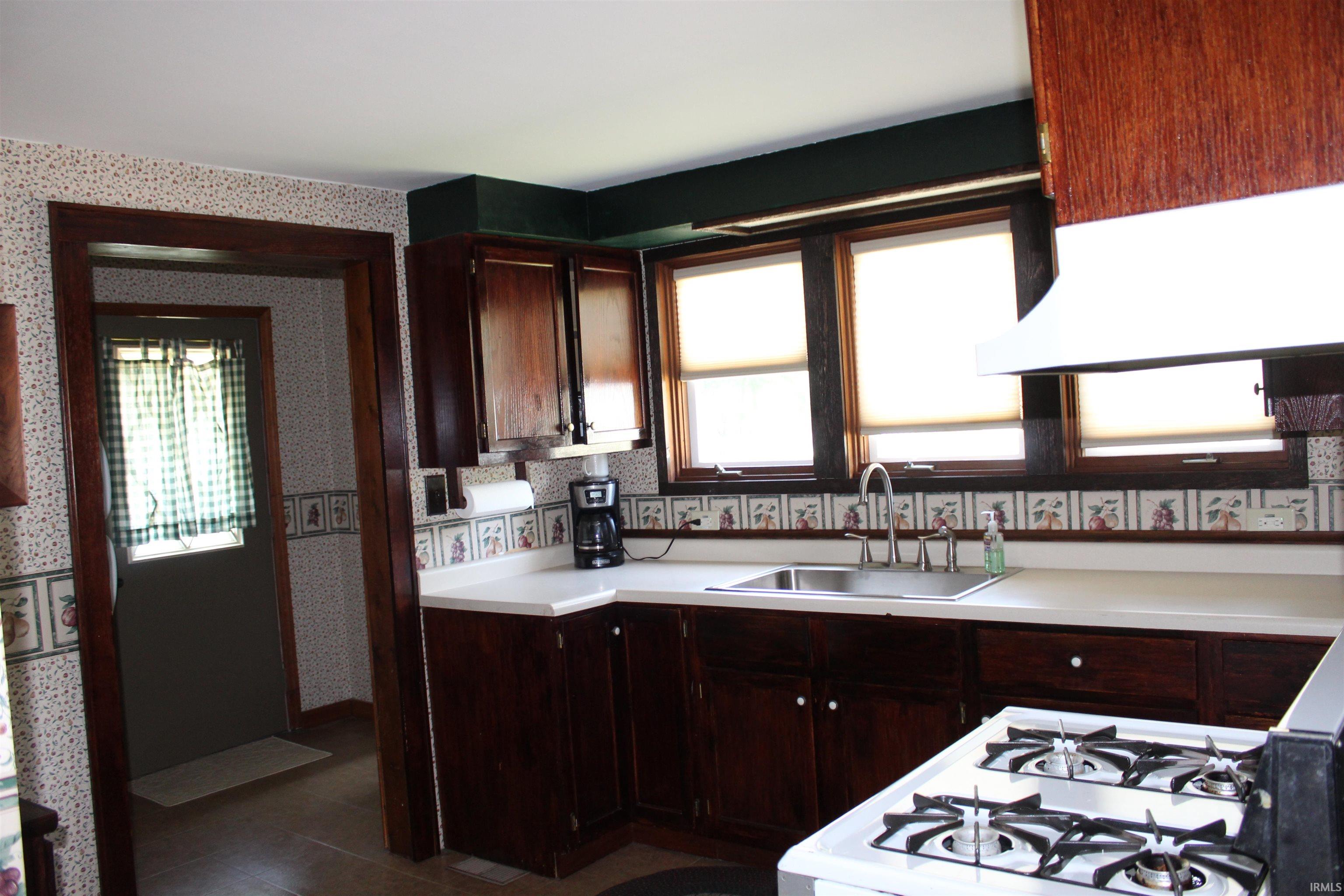 Kitchen featuring dark wood-finish cabinetry, white countertops, and a stainless steel sink with a gooseneck faucet