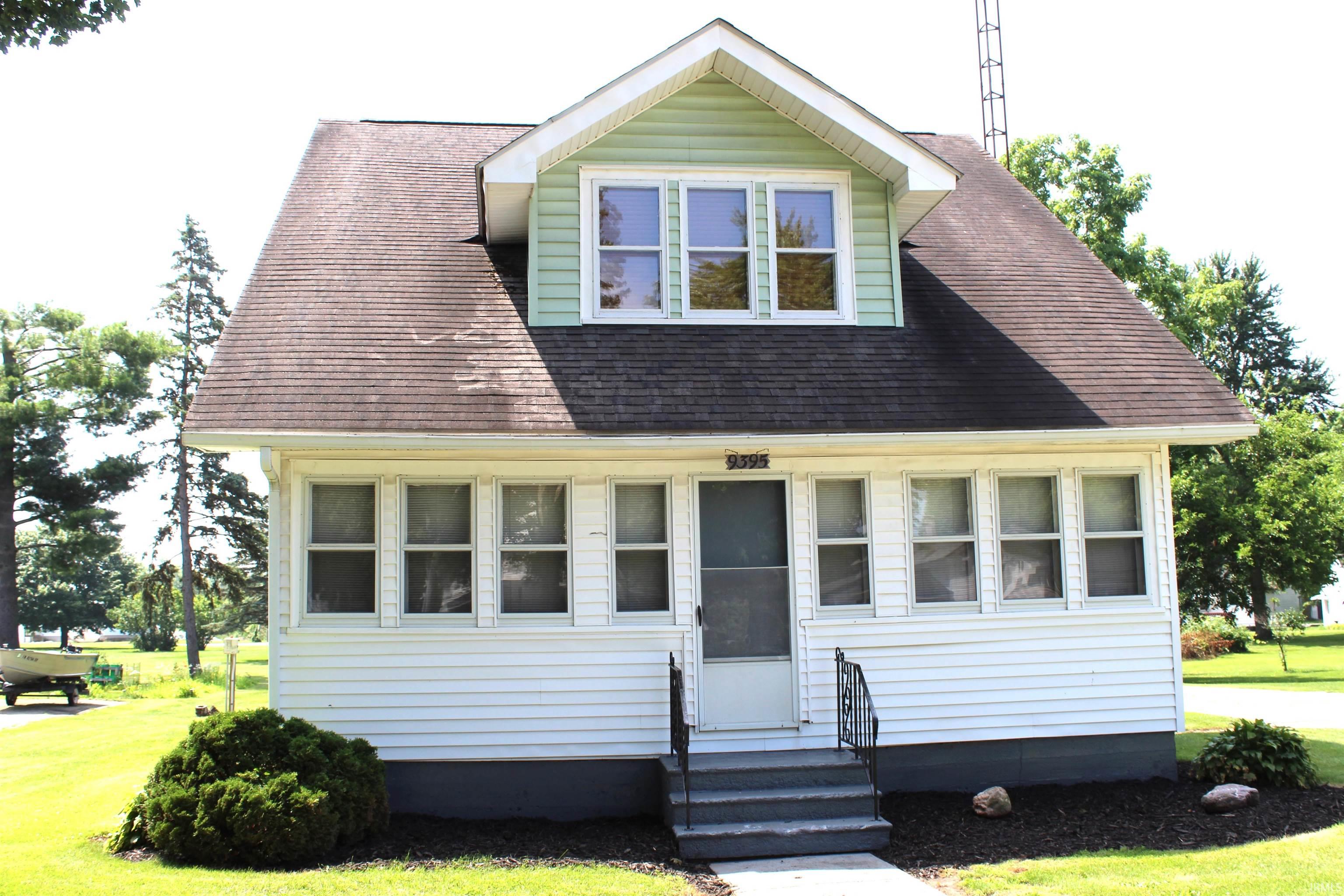 White siding exterior with a light green dormer, featuring a prominent front porch with multiple windows