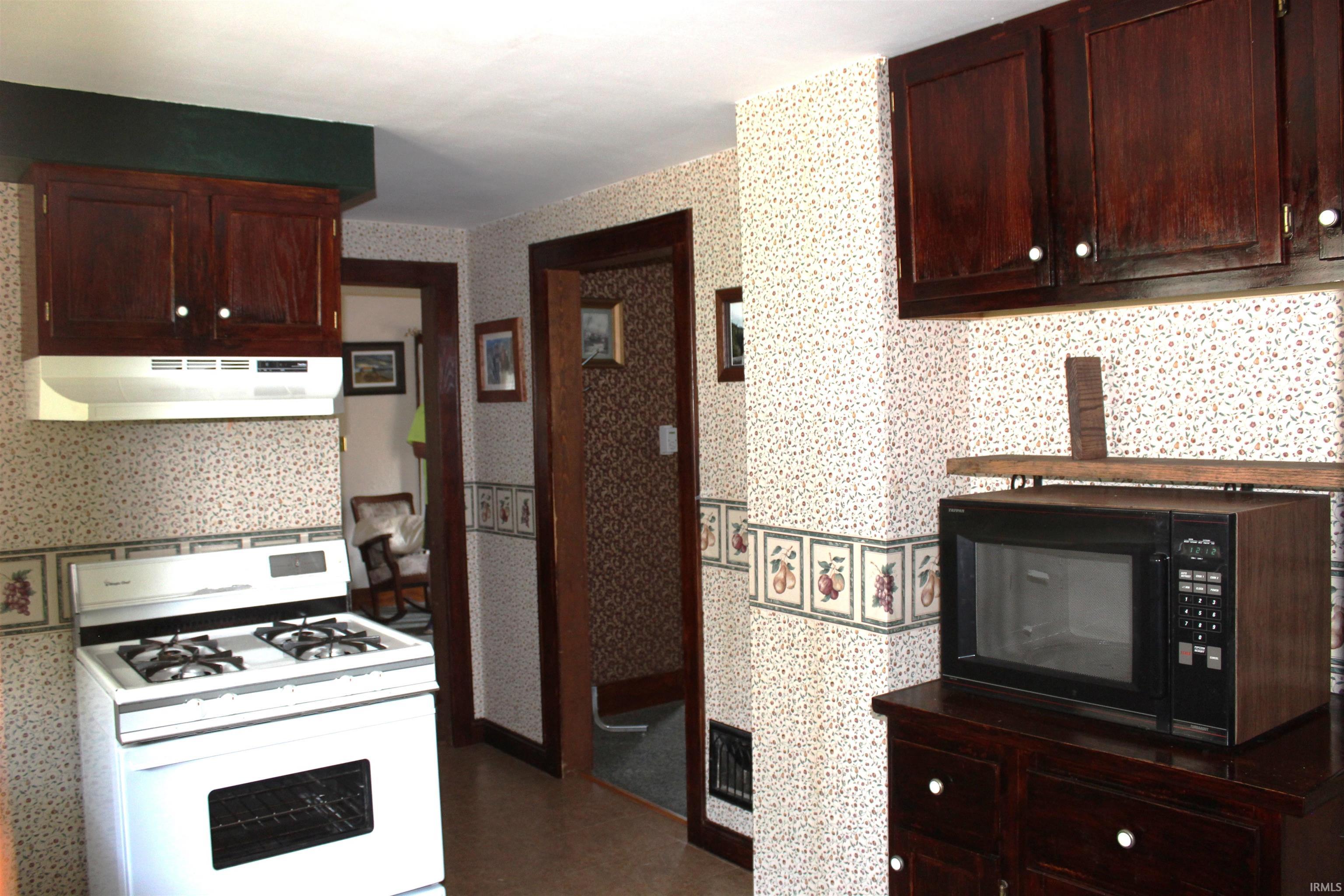 Kitchen featuring dark wood cabinetry, white gas range with range hood, and patterned wallpaper