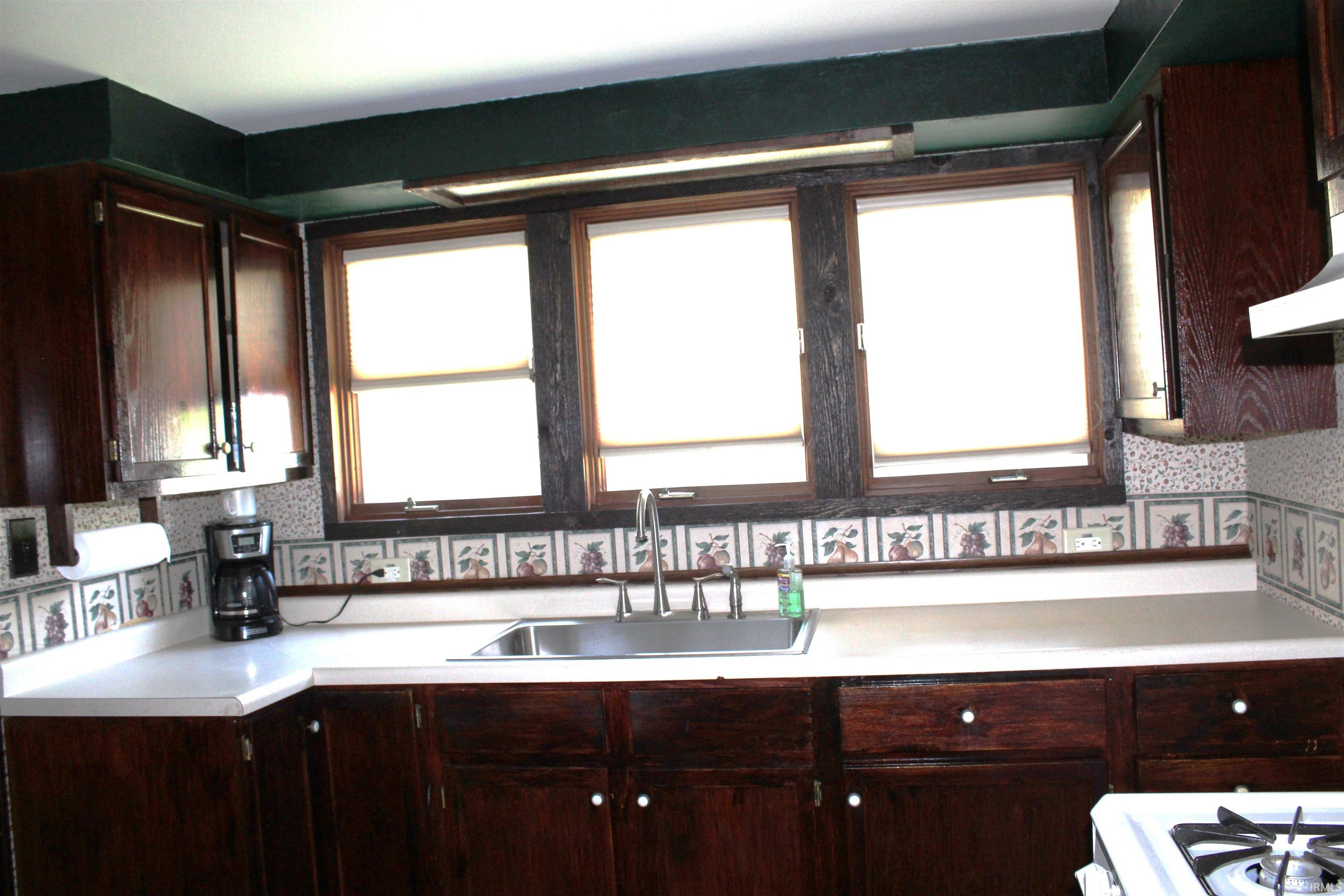 Kitchen workspace featuring dark wood cabinetry, light countertops, and a stainless steel sink with a gooseneck faucet