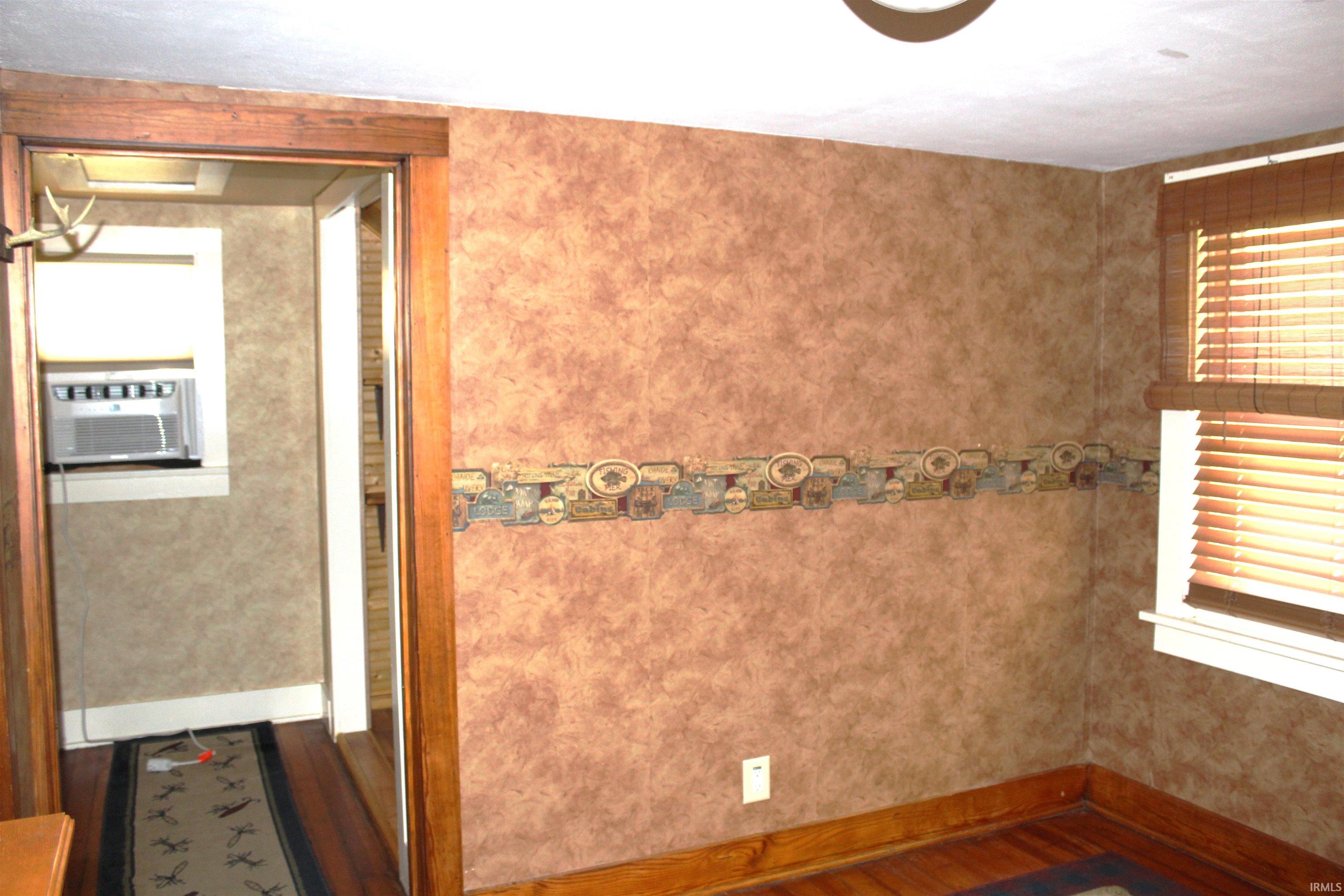 Room featuring textured wall treatment, a patterned border, and wood-finish flooring