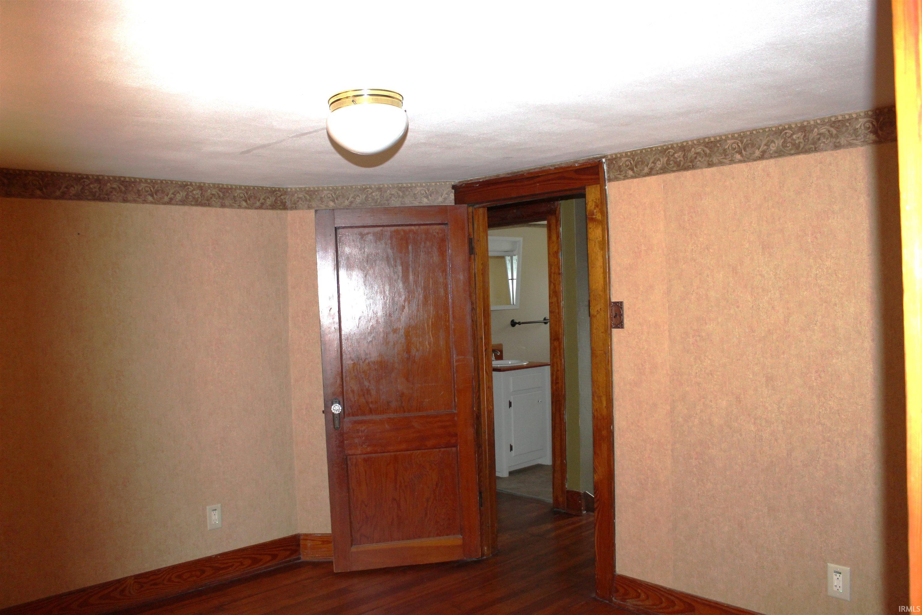 Room with wood-finish flooring, a paneled door, and a flush-mount ceiling light fixture