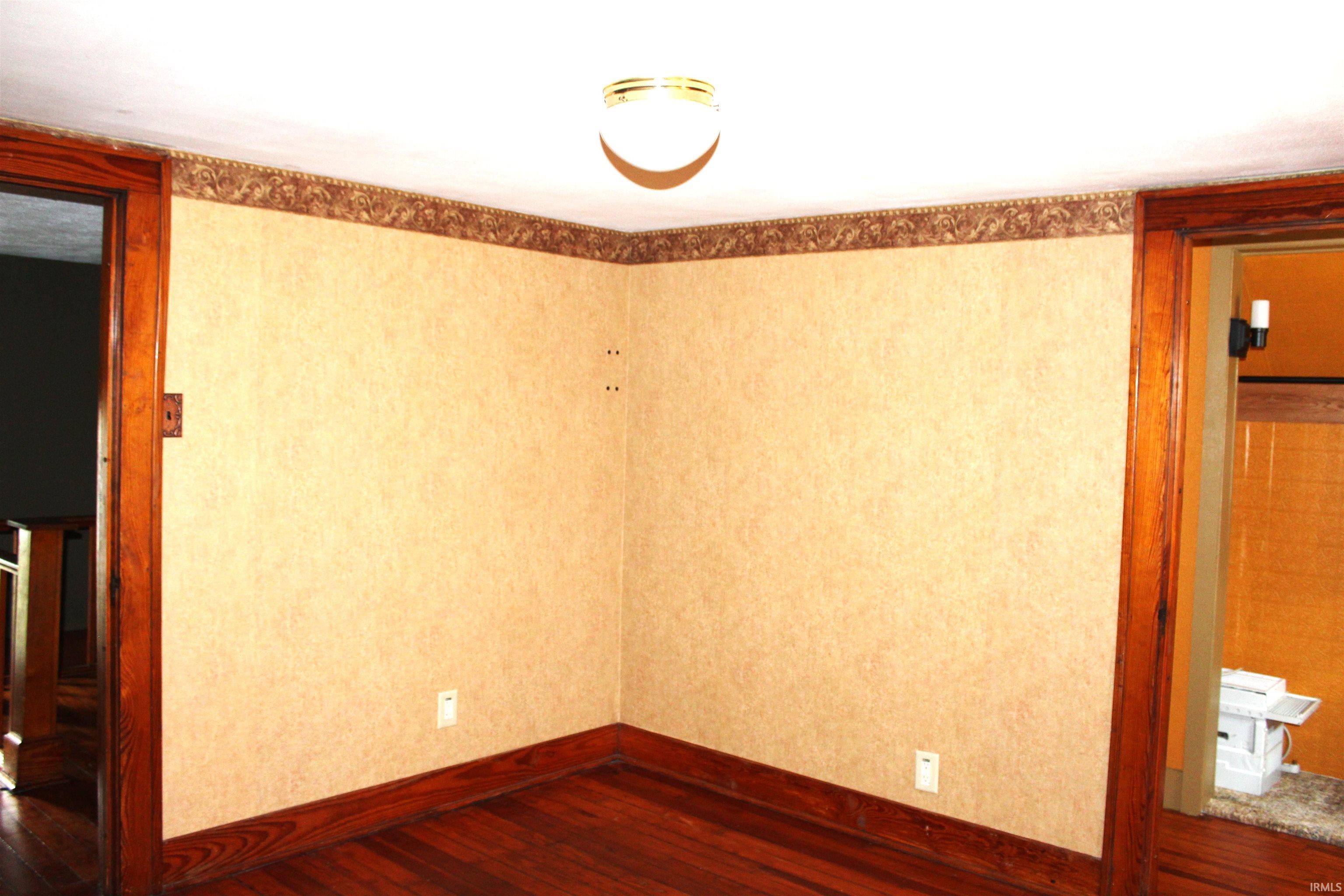 Room featuring wood-finish flooring, light-toned wallpaper, and a decorative border