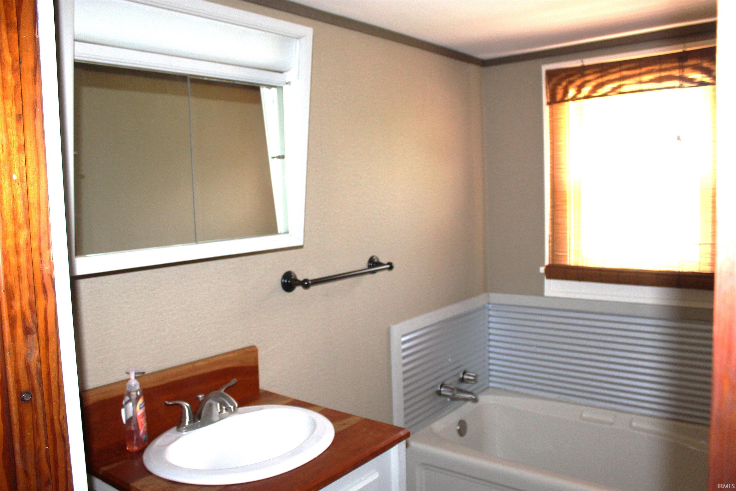 Bathroom featuring a white drop-in tub, corrugated metal wainscoting, and a window with a woven wood shade