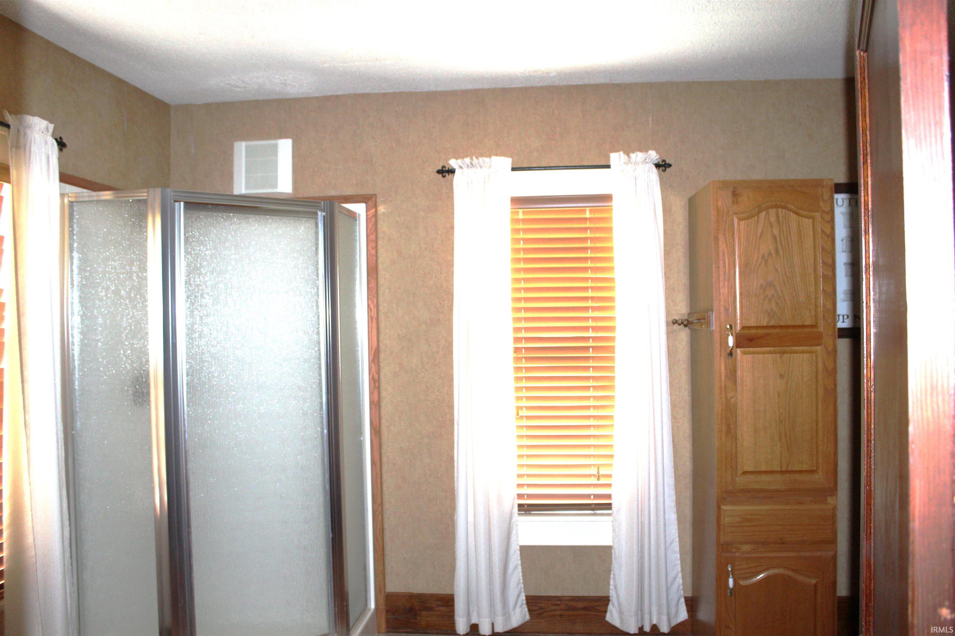 Shower enclosure with frosted glass panels, adjacent to a built-in wood cabinet, and a window with blinds
