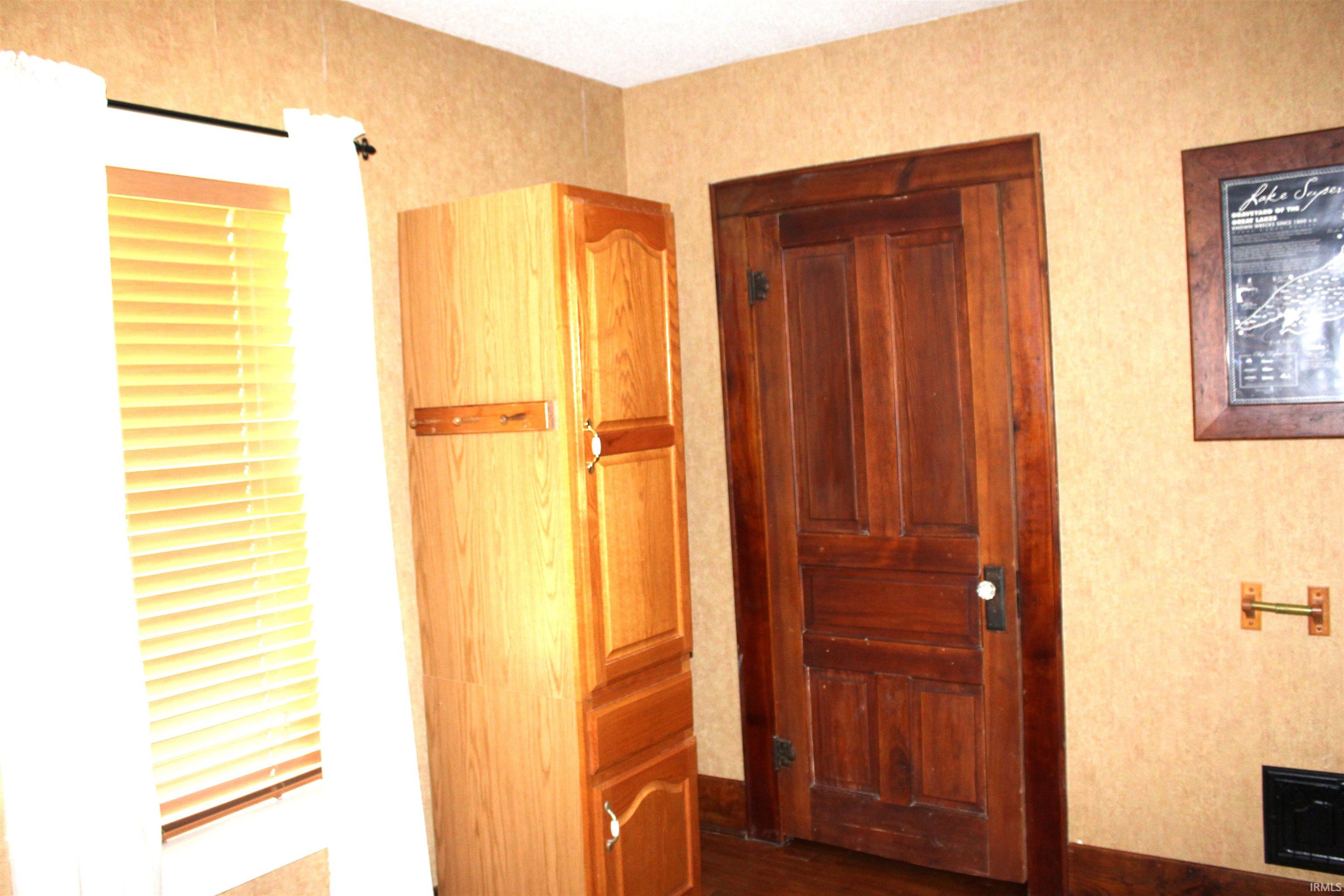 Wood-finish flooring with a paneled wood door and wood-framed window featuring blinds