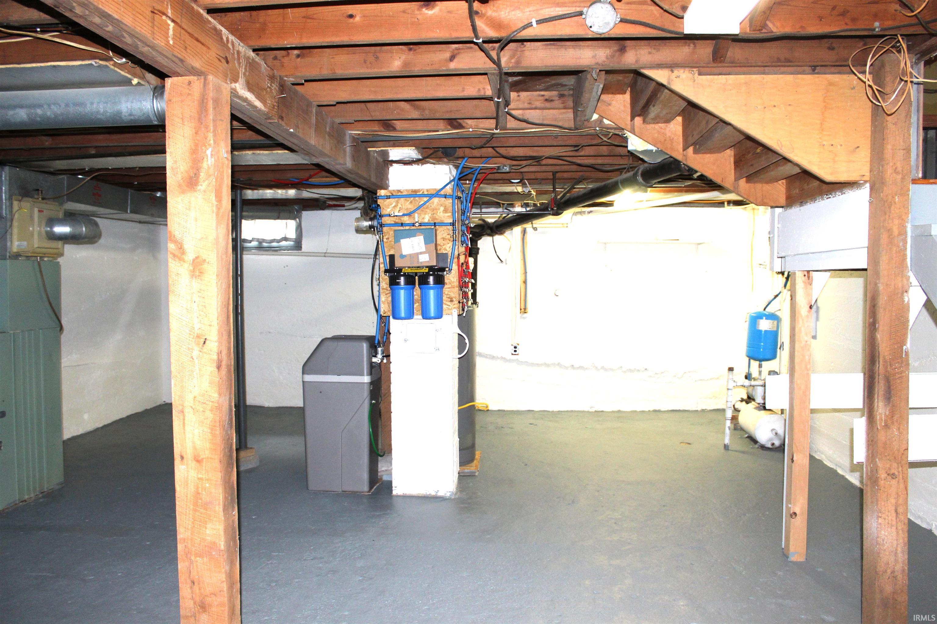 Open basement space with painted concrete flooring, exposed wood beam ceiling, white-painted foundation walls, and various utility systems