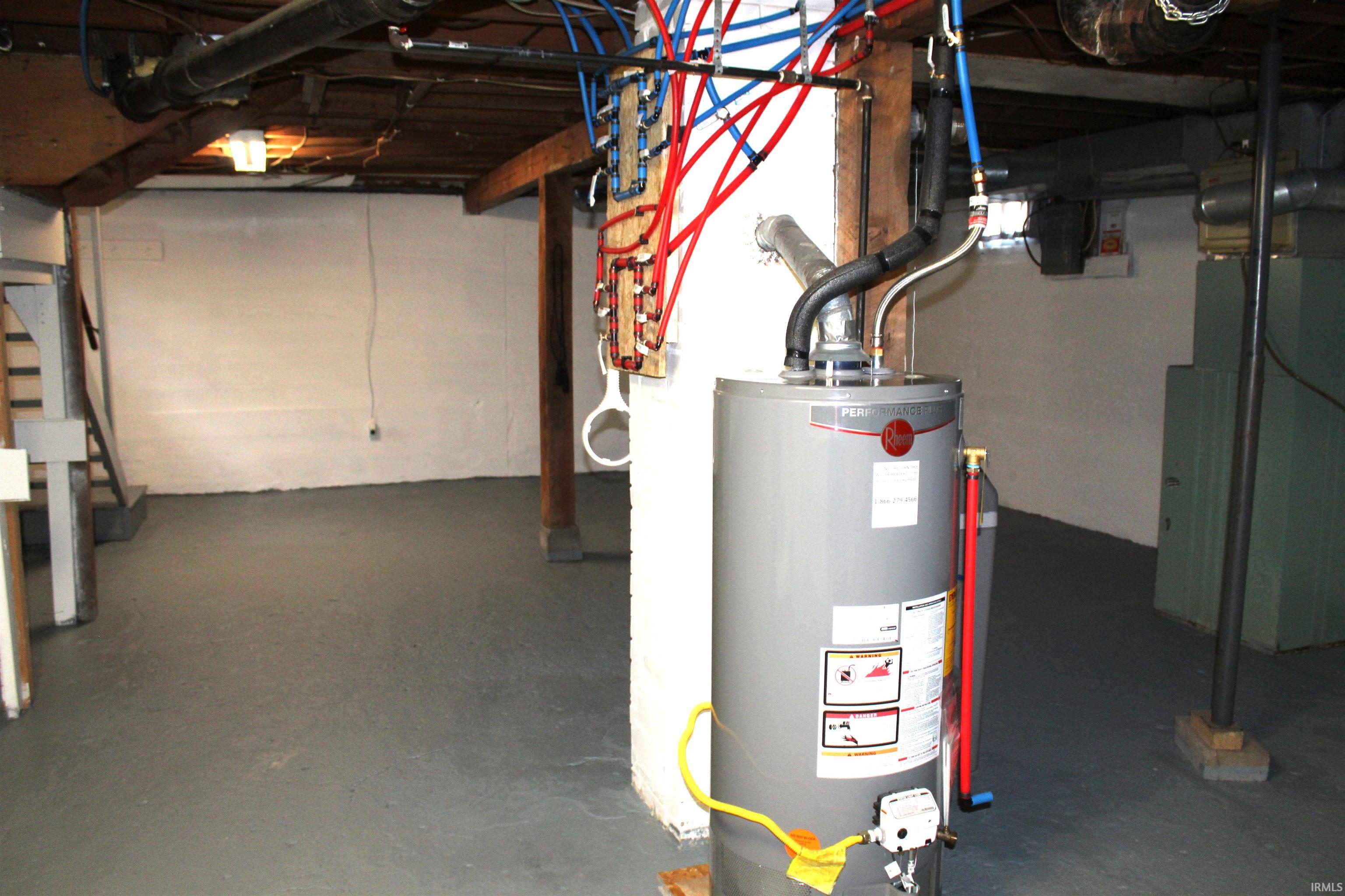 Utility room featuring a water heater, exposed overhead plumbing, and painted concrete flooring