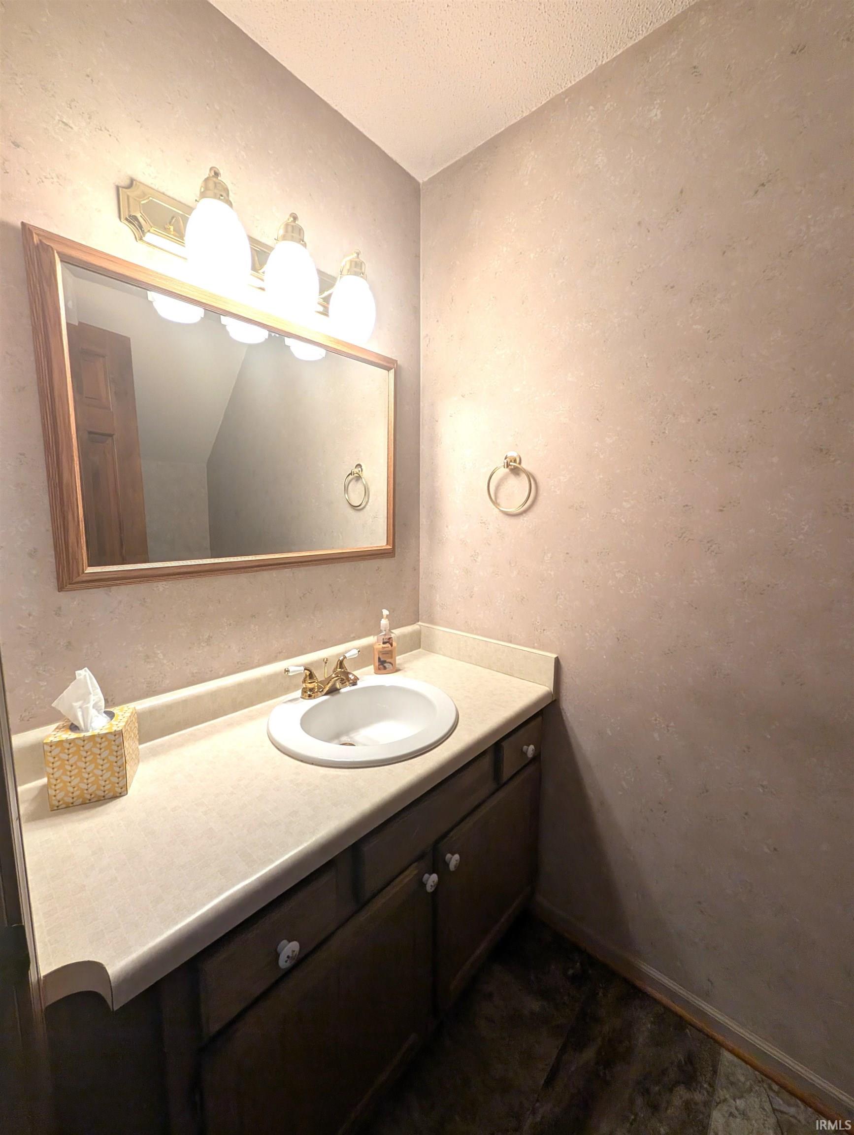 Bathroom vanity featuring a gold-finish faucet, an undermount sink, and a light-toned countertop