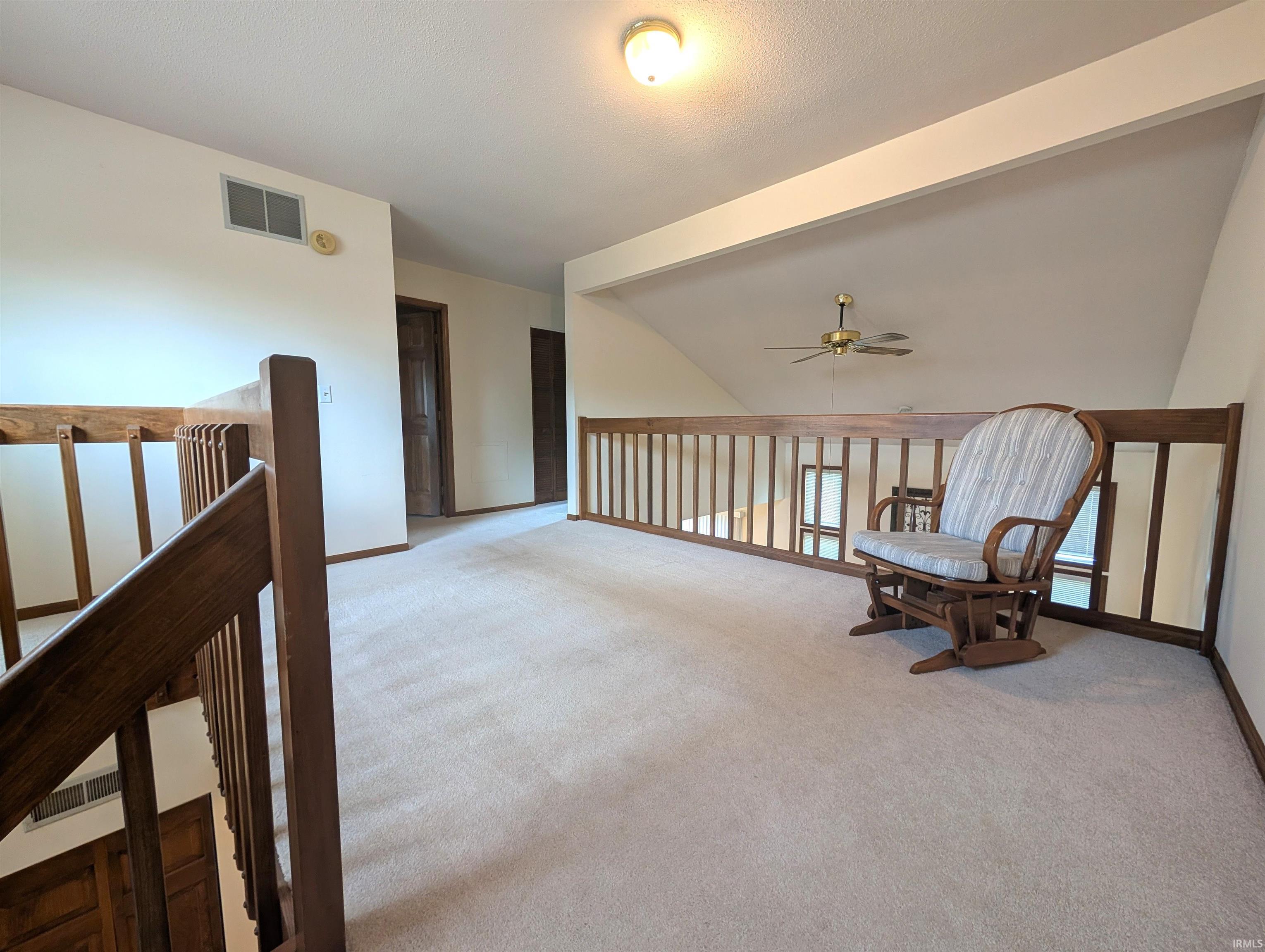 Carpeted loft area featuring wood railings, a ceiling fan, and recessed walls