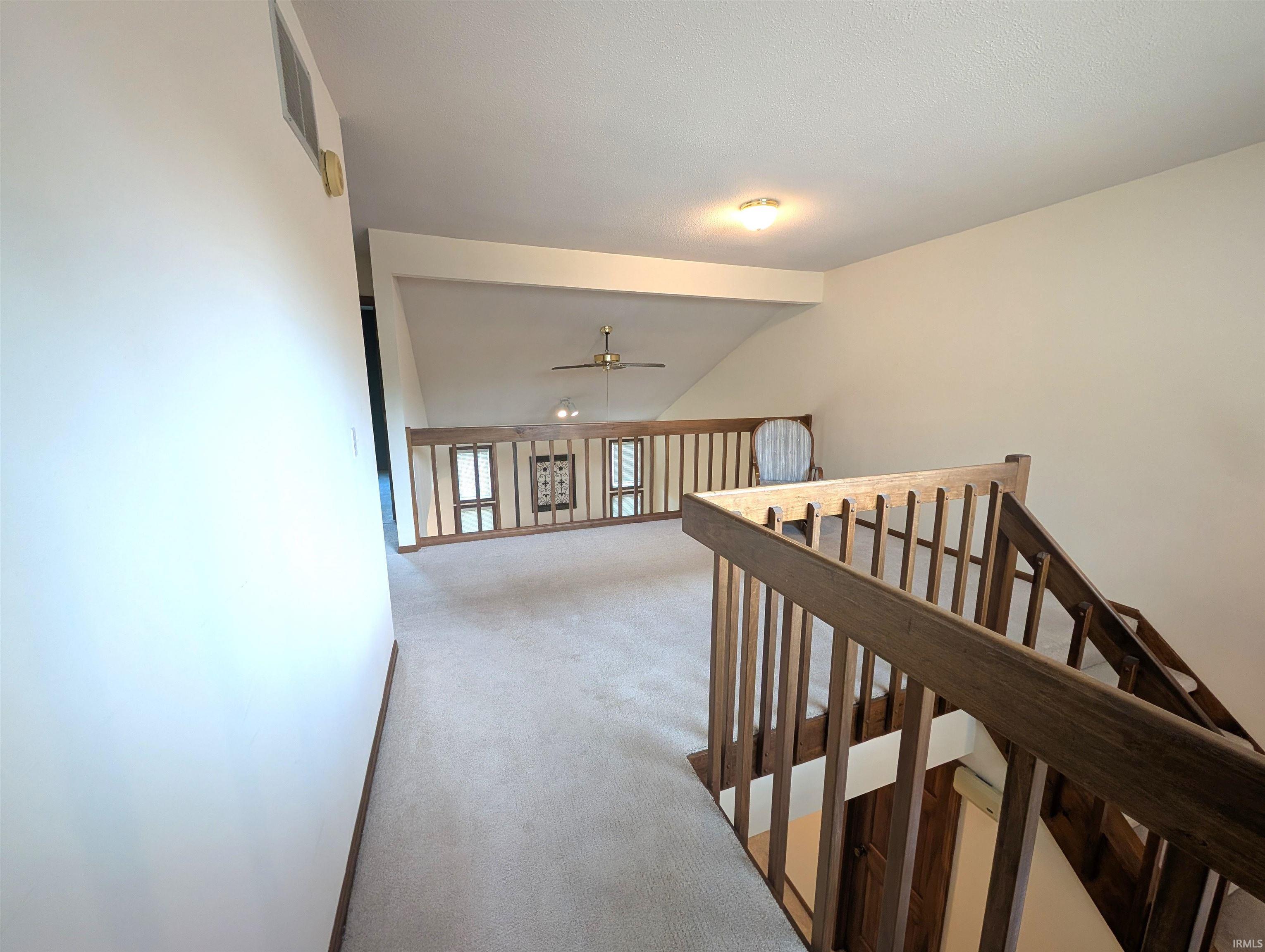 Loft area with carpet flooring, wood balustrade, and a ceiling fan