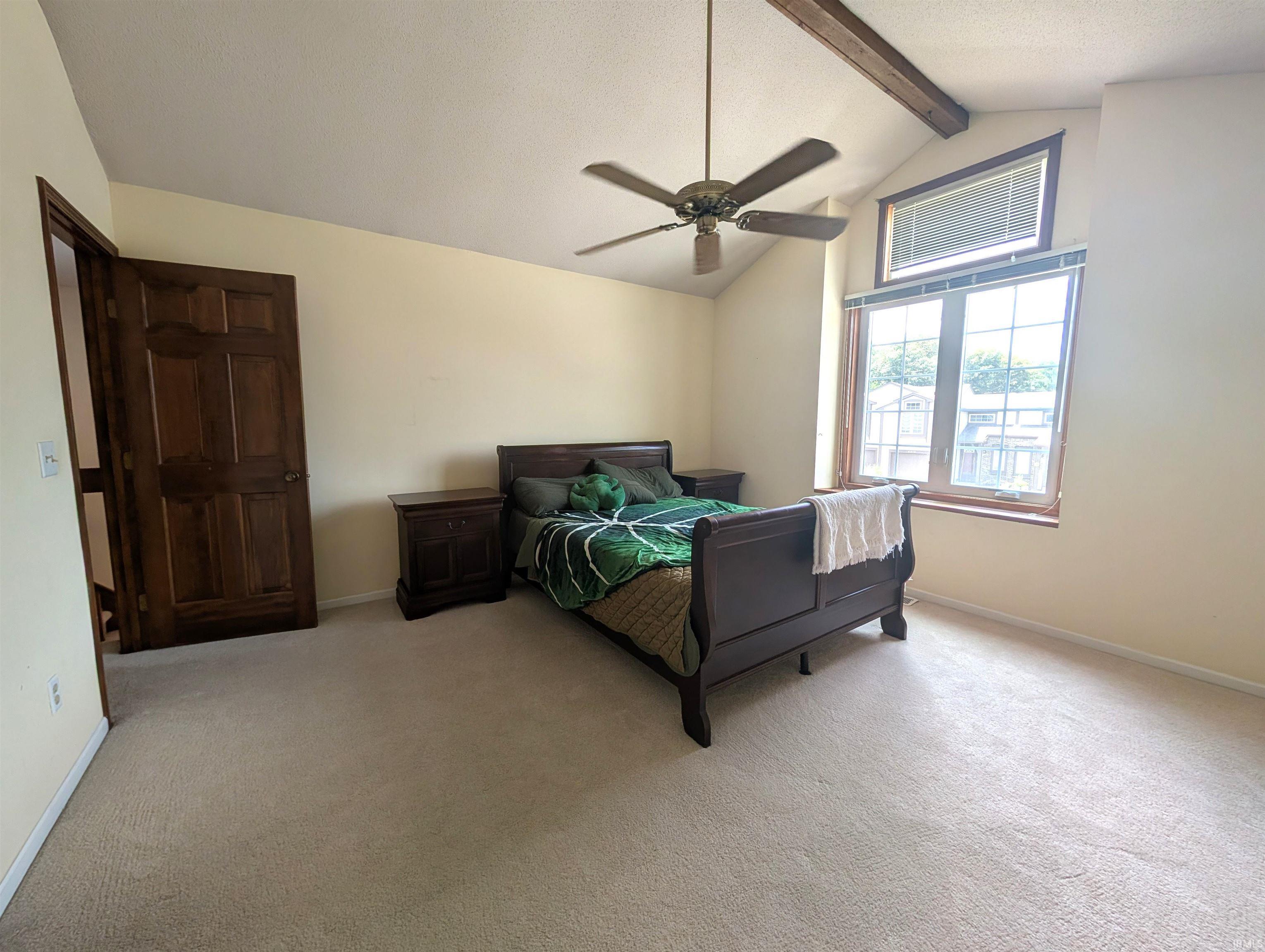 Bedroom featuring vaulted ceilings with exposed wood beams, a transom window, a large picture window, and neutral carpeting