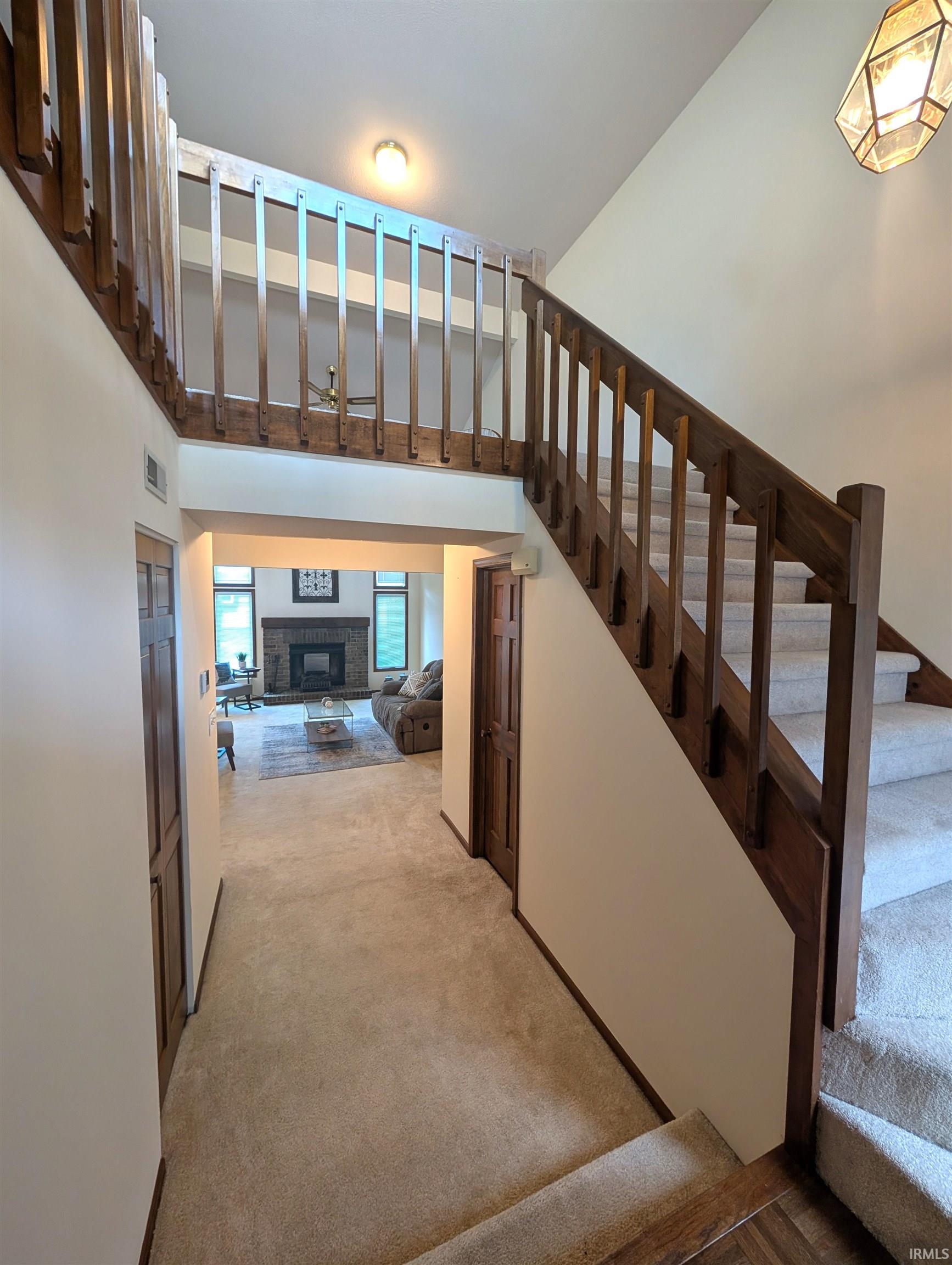 Central staircase with wood-finish railing and carpeted treads, featuring a two-story entry and an open balcony overlooking the lower level