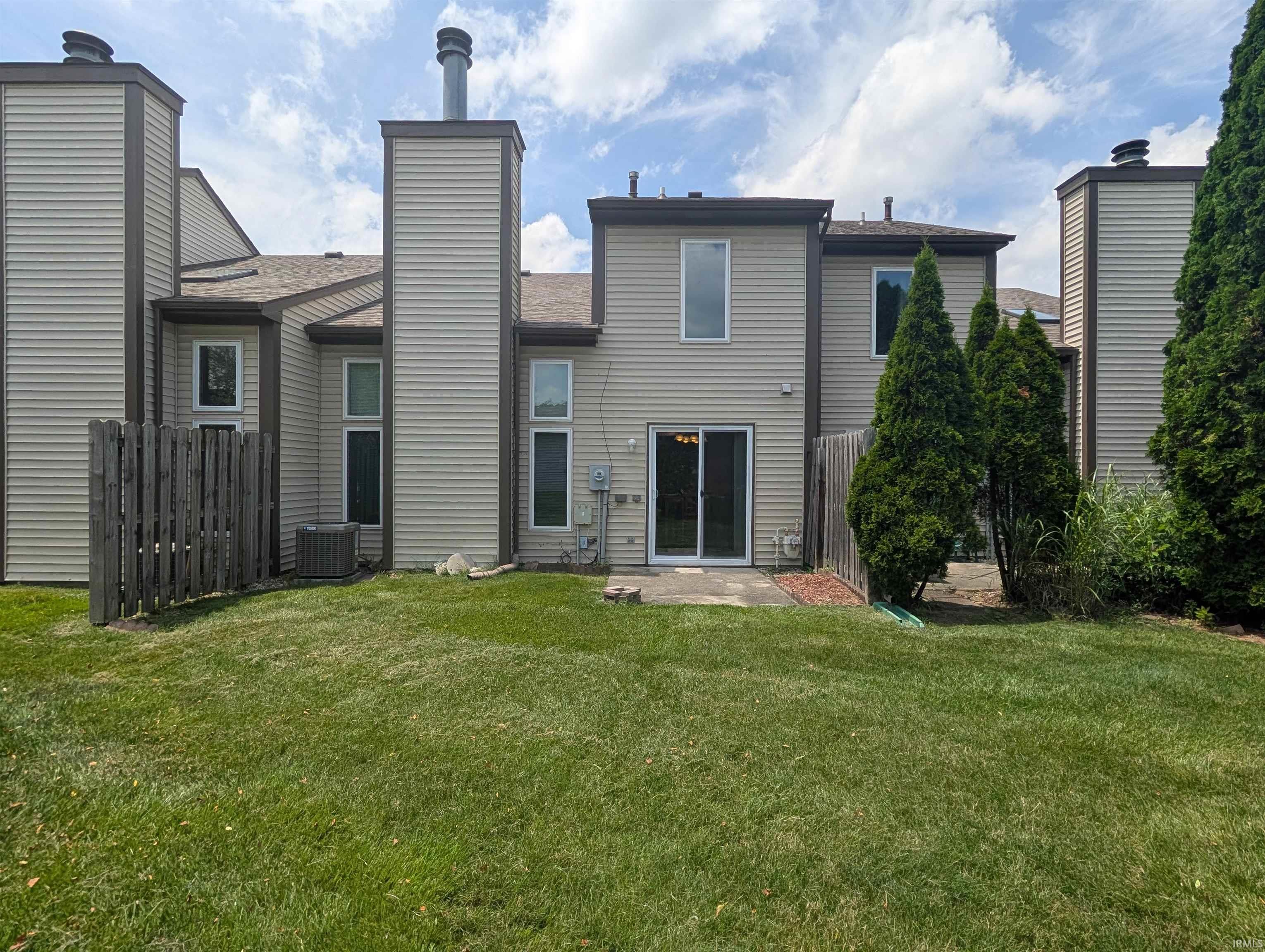 Rear exterior featuring horizontal siding, multiple tall windows, two chimneys, a ground-level patio, and a sliding glass door