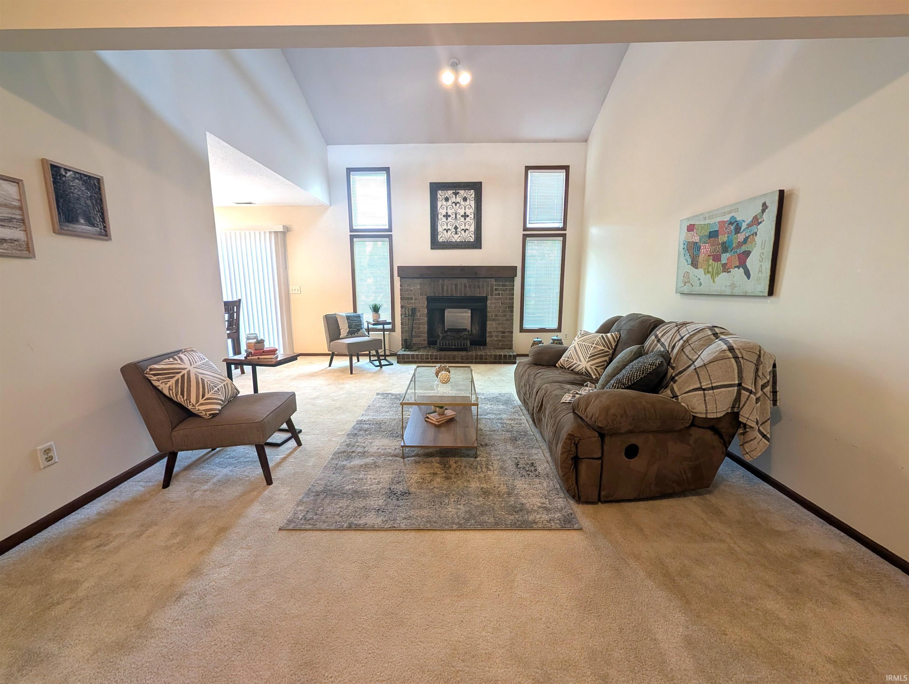 Living area featuring a brick fireplace, vaulted ceiling, and multiple windows