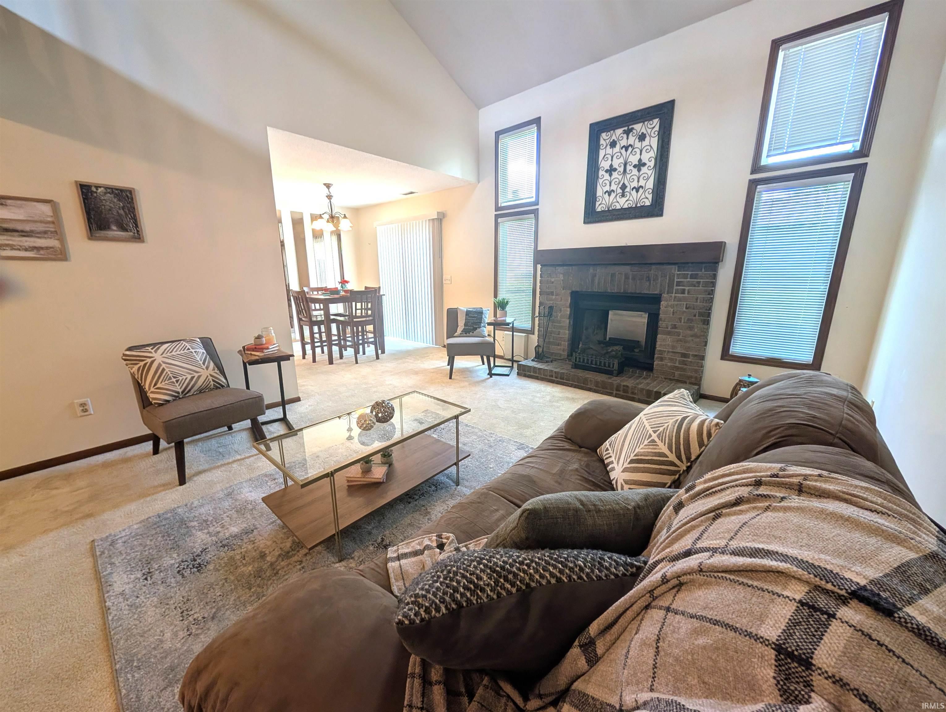 Vaulted ceiling living area featuring a brick-surround fireplace with a wood mantle, angled windows, and carpet flooring